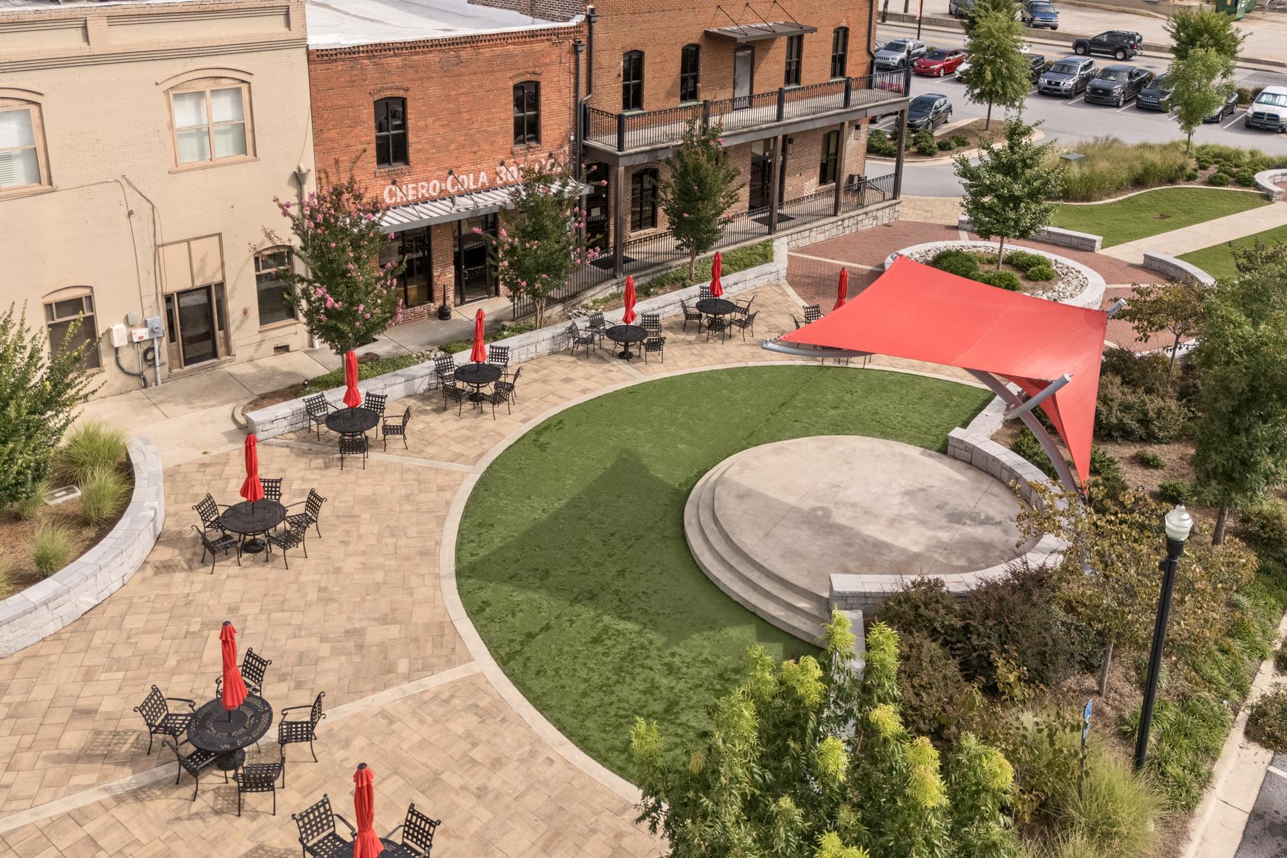 Outdoor plaza at Lake Shore in Winder Georgia with red umbrella tables, central pavilion, brick buildings, and green landscaping