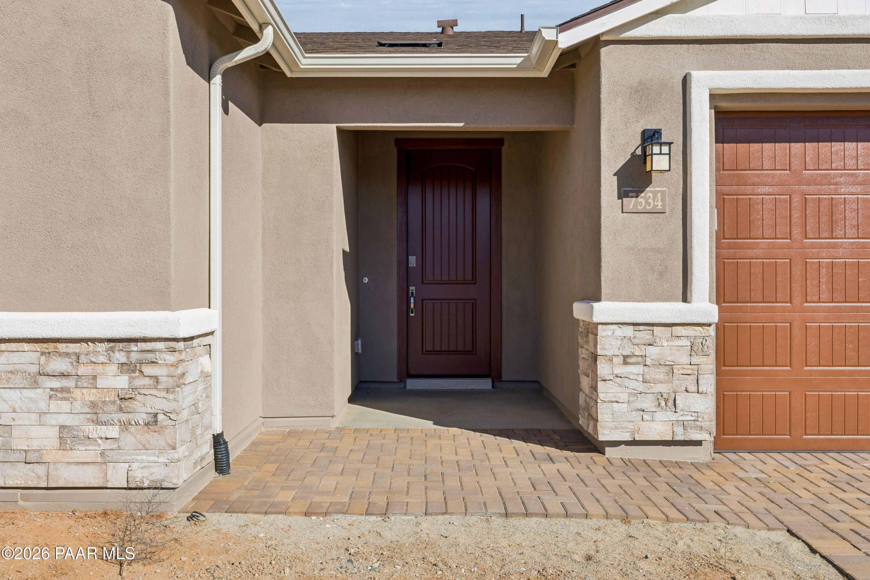 Modern beige stucco home exterior with dark wood front door, stone accents, lantern light, and three-car garage in Davidson Homes The Harmony A, Prescott Valley, Arizona