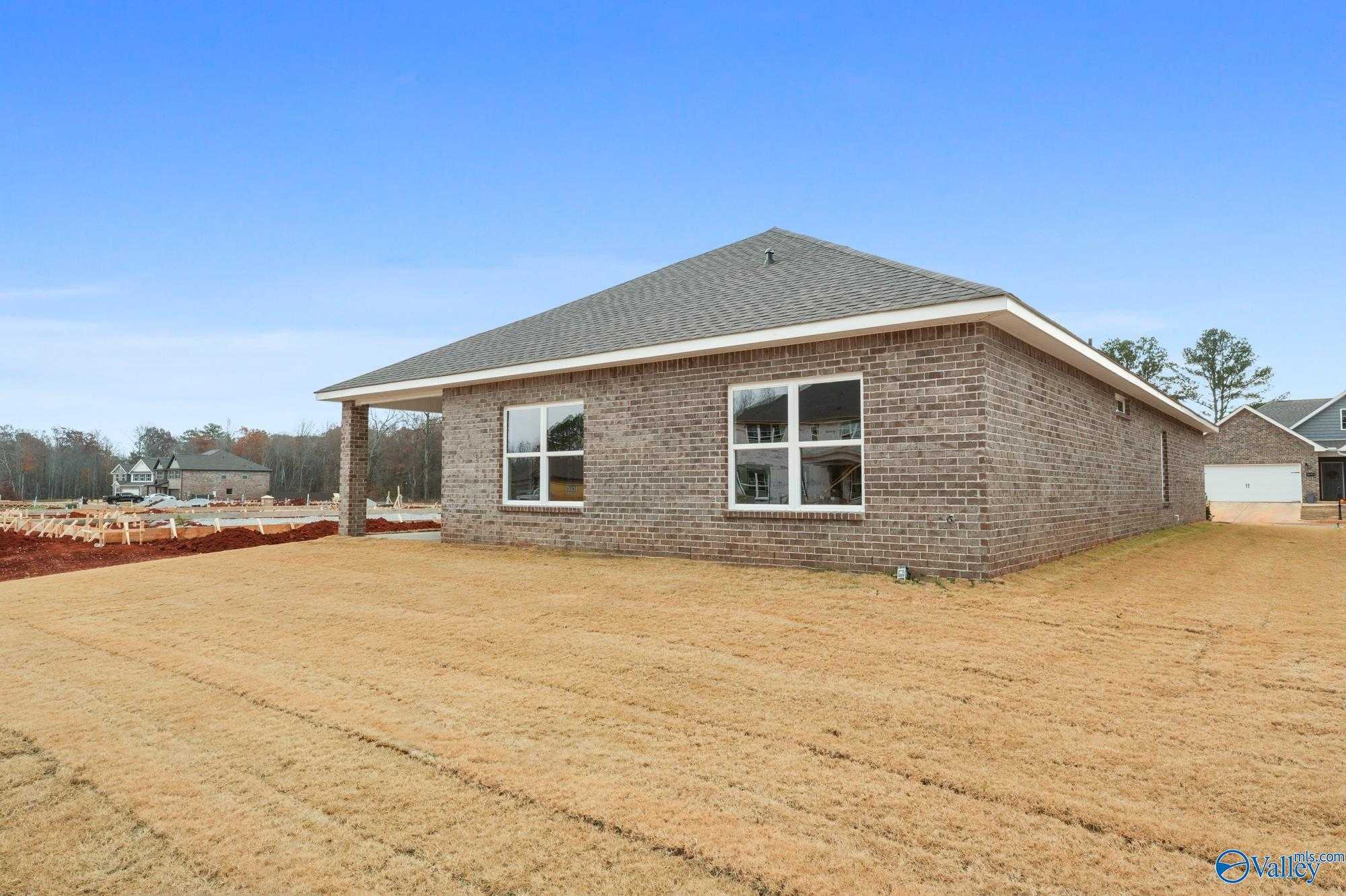 Side view of single-story brick Daphne D home with gable roof, large windows, two-car garage, covered porch, and new sod yard in Ricketts Farm, Athens, Alabama
