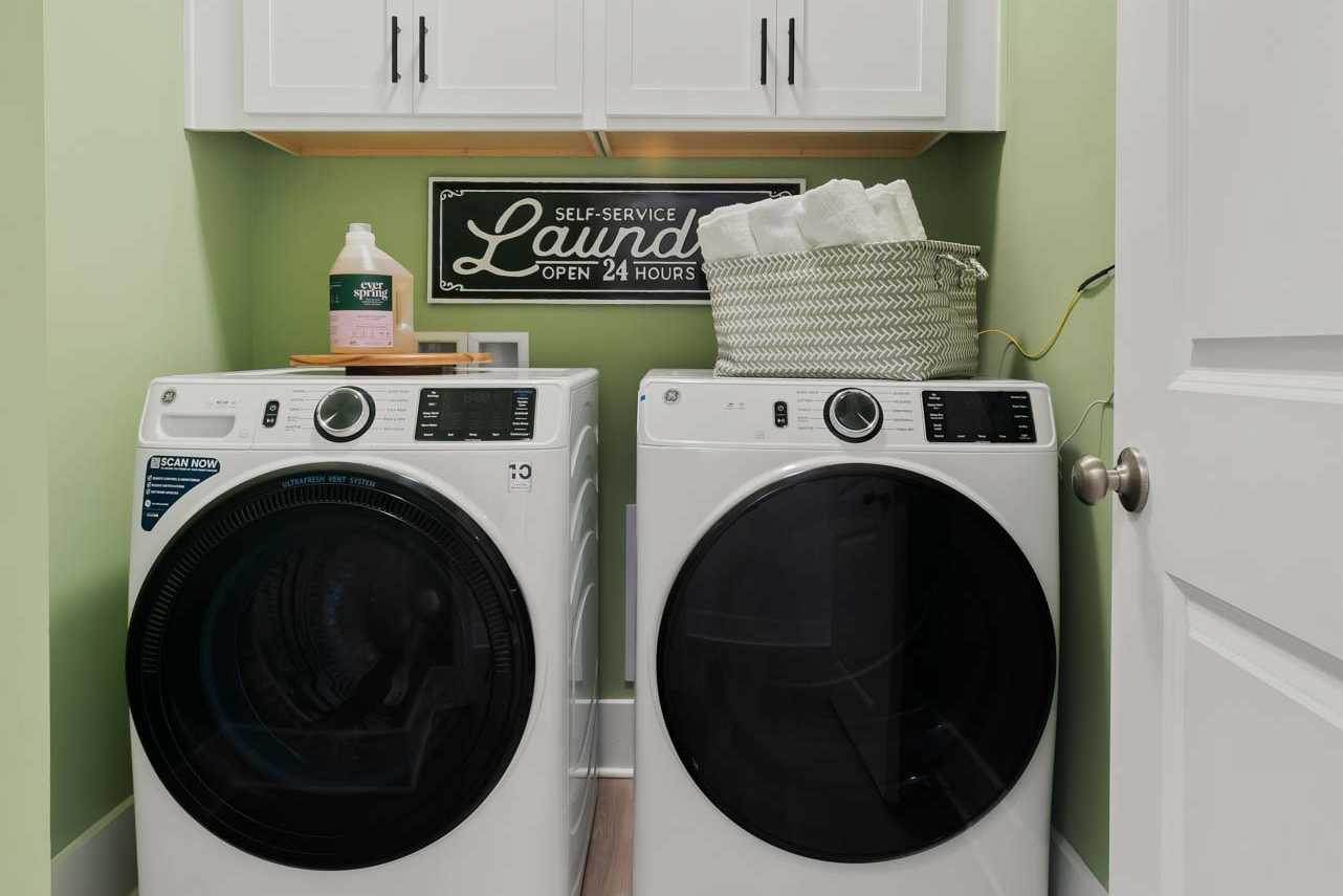 Modern laundry room in Durham Farms Harvest Alabama with white front-load washer dryer green walls wood floors