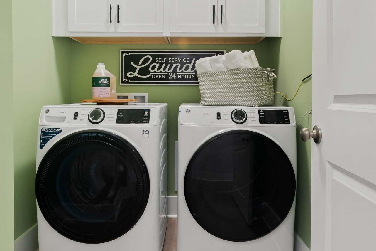 Modern laundry room in Durham Farms Harvest Alabama with white front-load washer dryer green walls wood floors