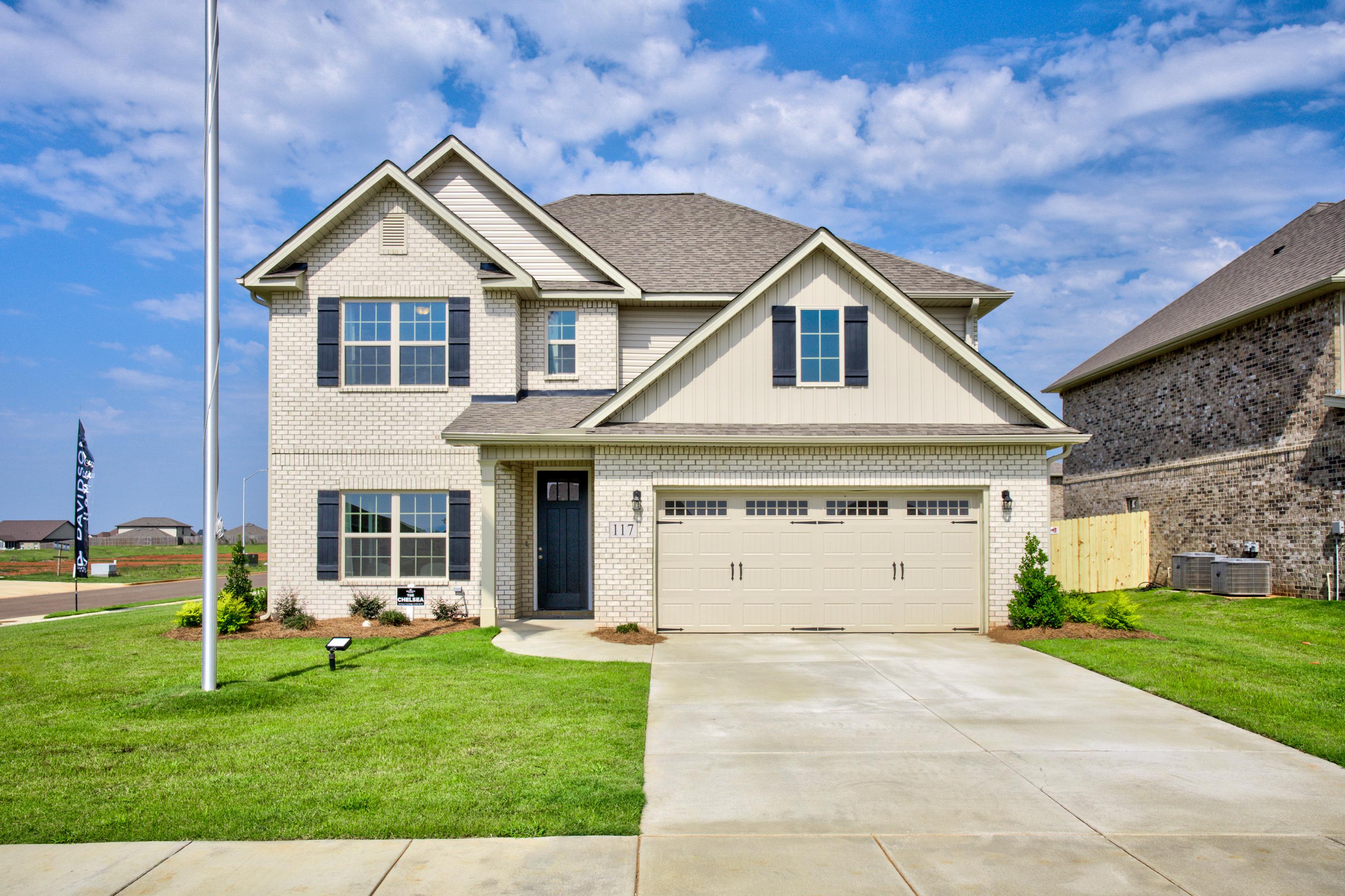 Two-story Chelsea A home elevation with beige brick siding, gabled roof, two-car garage, and manicured lawn in Meridianville