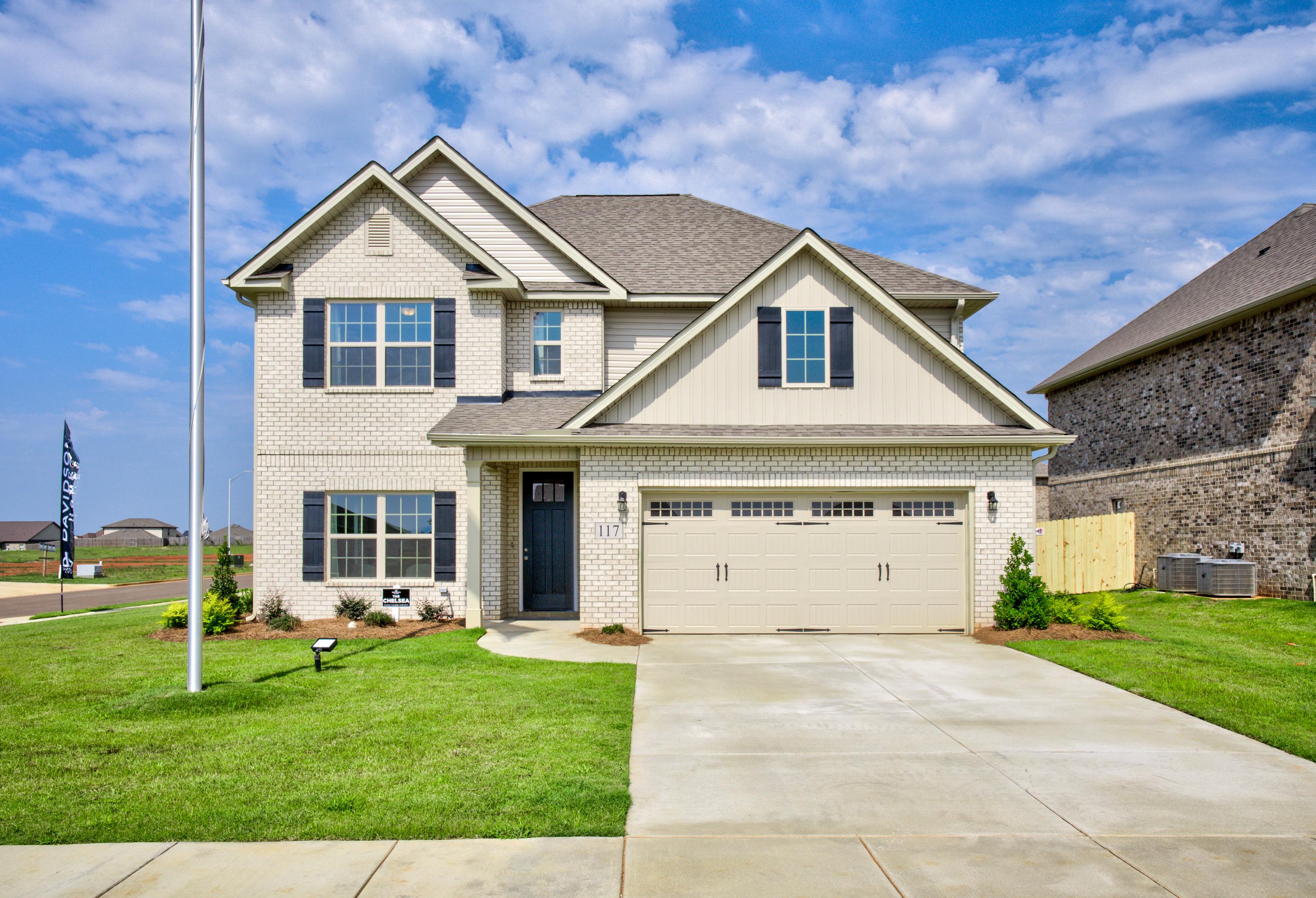 Two-story Chelsea A home elevation with beige brick siding, gabled roof, two-car garage, and manicured lawn in Meridianville