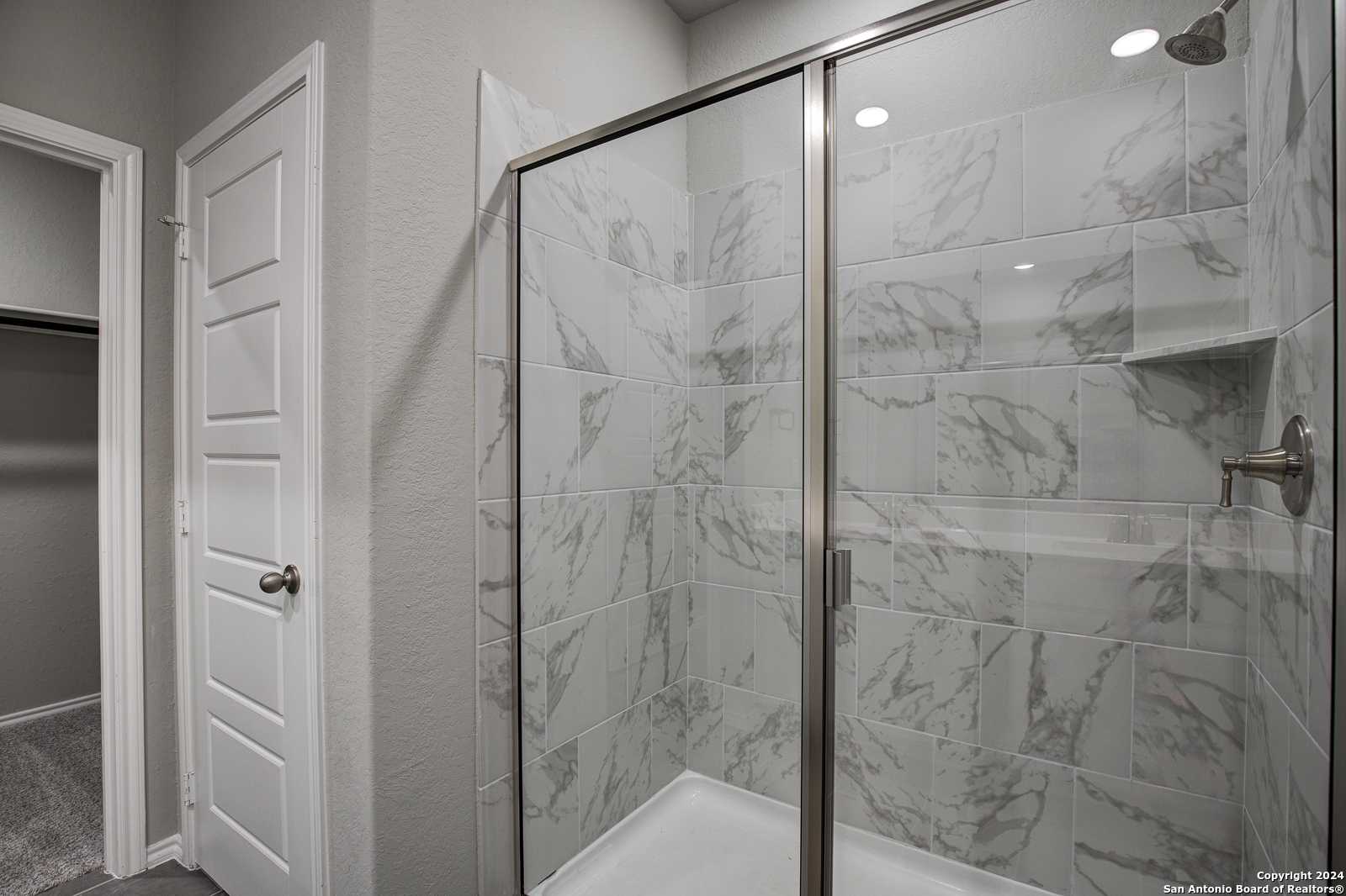 Modern master bathroom featuring frameless glass walk-in shower with marble-look tiles in Davidson Homes The Daphne J, Seguin, Texas