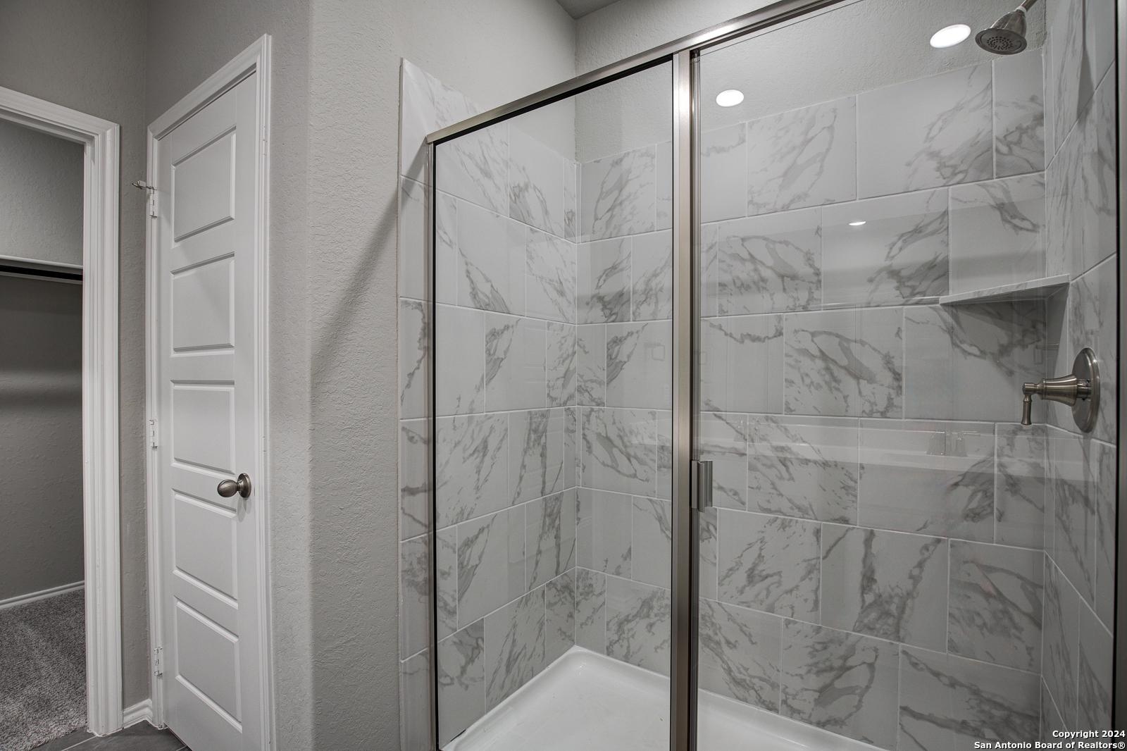 Modern master bathroom featuring frameless glass walk-in shower with marble-look tiles in Davidson Homes The Daphne J, Seguin, Texas