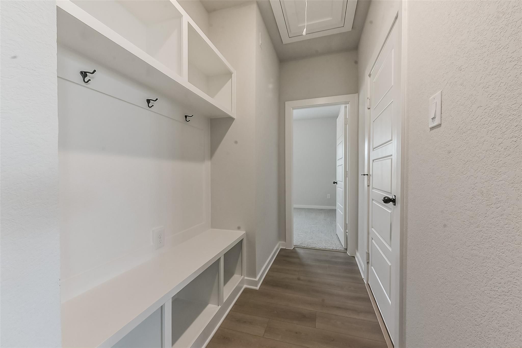 White mudroom with built-in white cabinetry, coat hooks, bench, and open shelves in Davidson Homes The Everett C, Crosby, Texas