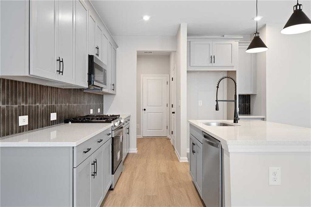 Modern kitchen with white shaker cabinets, stainless steel appliances, large island sink, and hardwood floors in Davidson Homes The Marion A, Kennesaw, GA