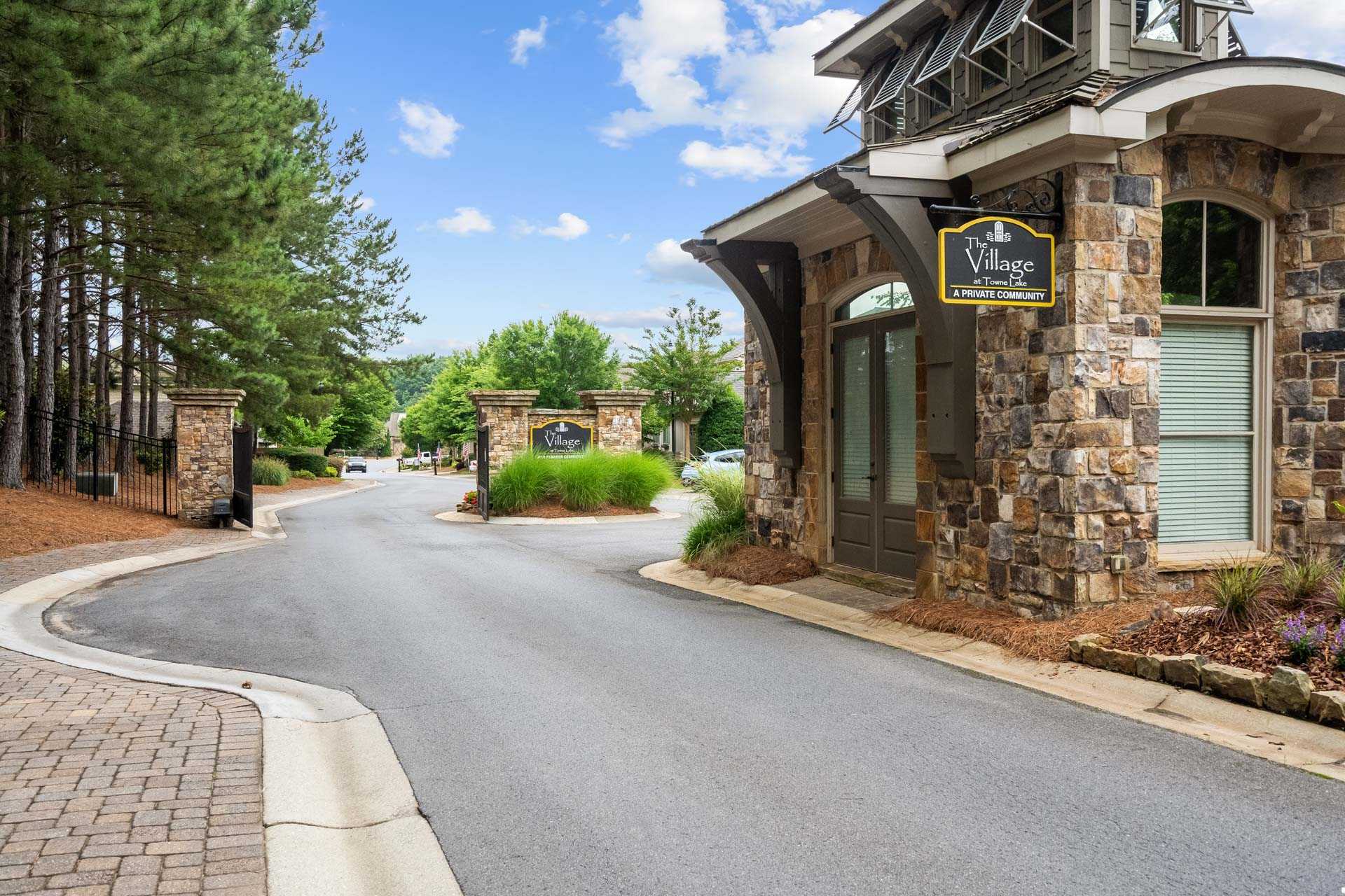 Stone archway gated entrance at The Village at Towne Lake in Woodstock GA with pine trees and landscaped road