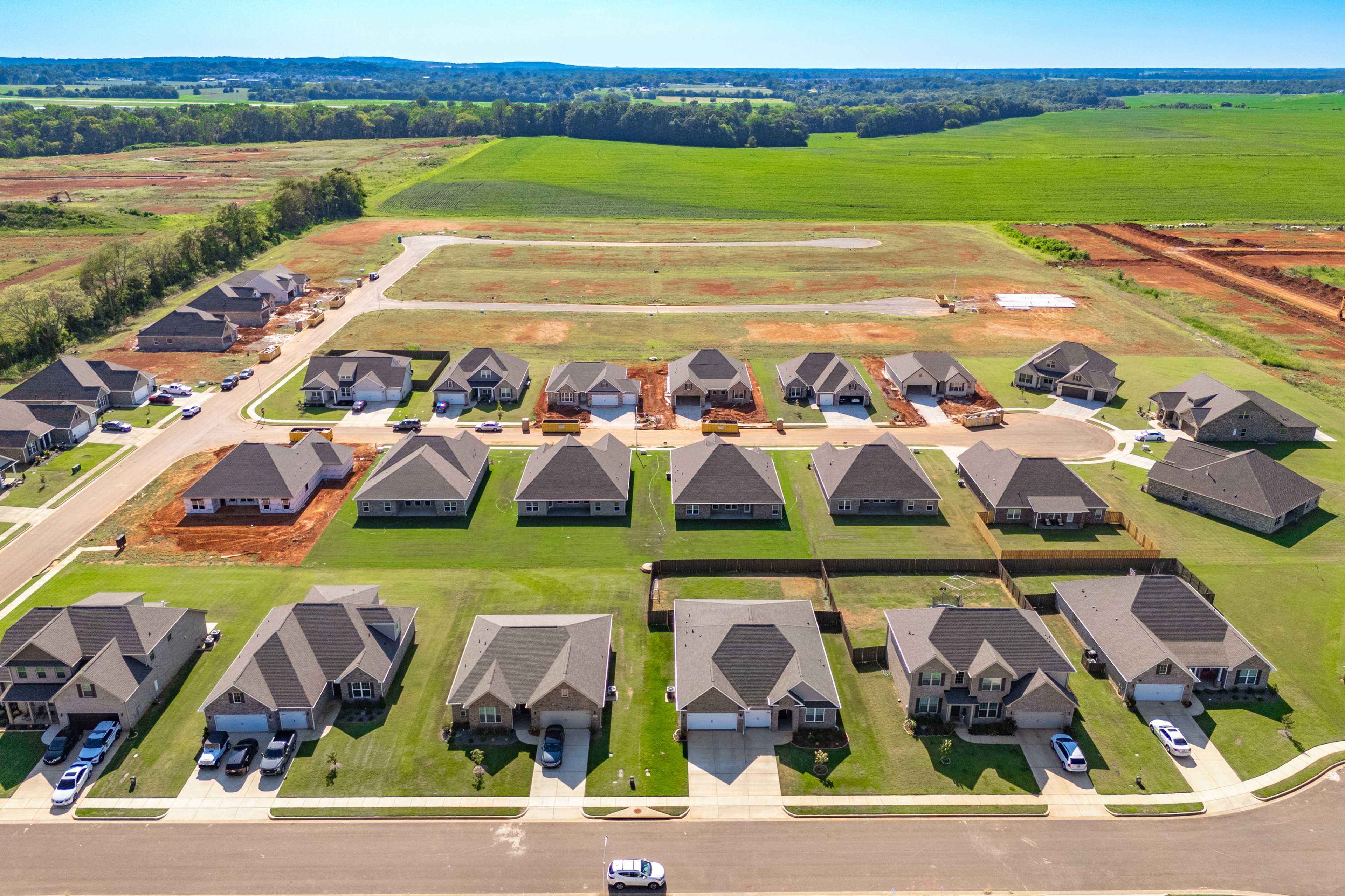 Aerial view of Pikes Ridge neighborhood in Meridianville Alabama featuring new single-family homes with garages amid green lawns and fields