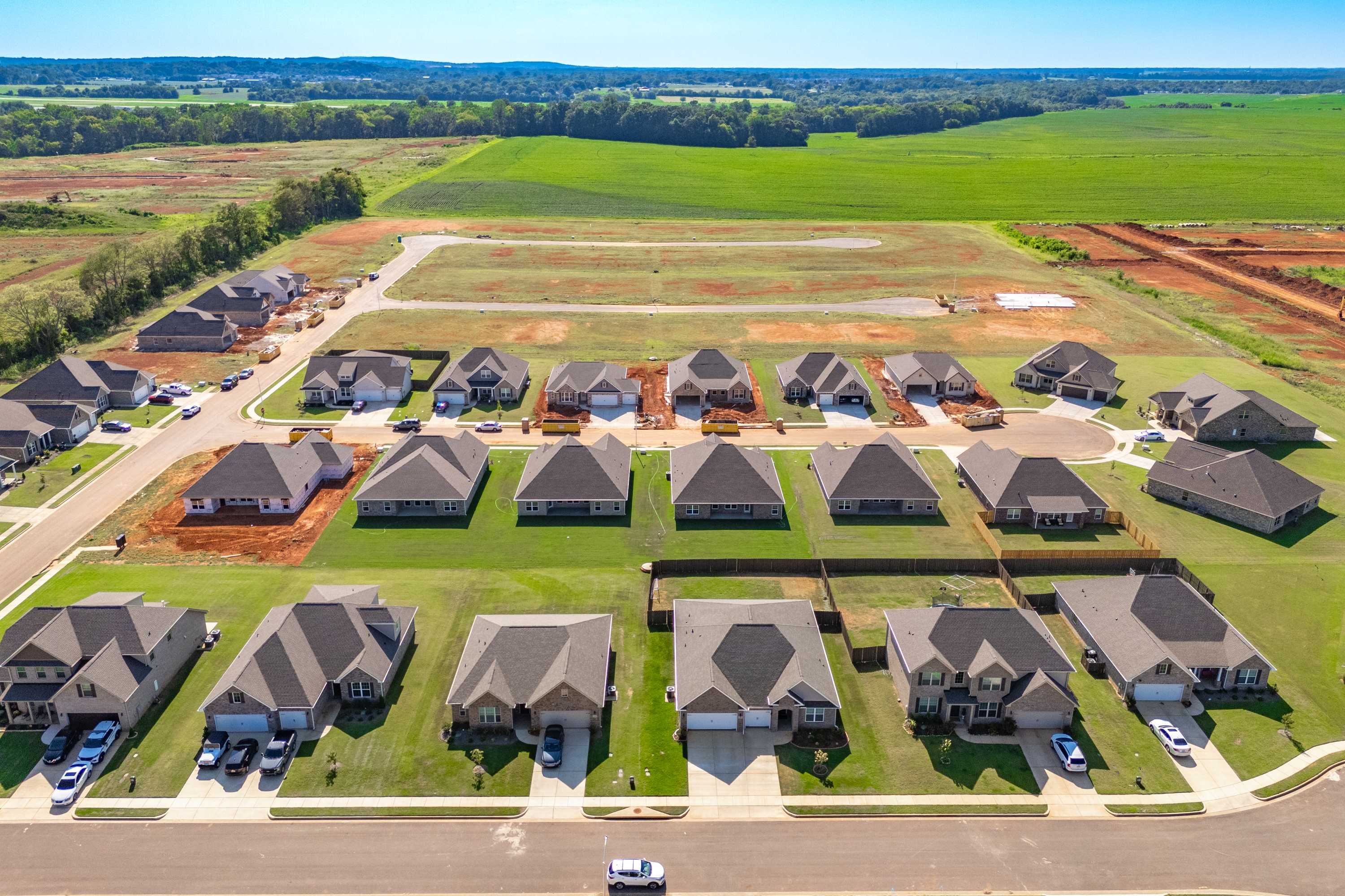 Aerial view of Pikes Ridge neighborhood in Meridianville Alabama featuring new single-family homes with garages amid green lawns and fields