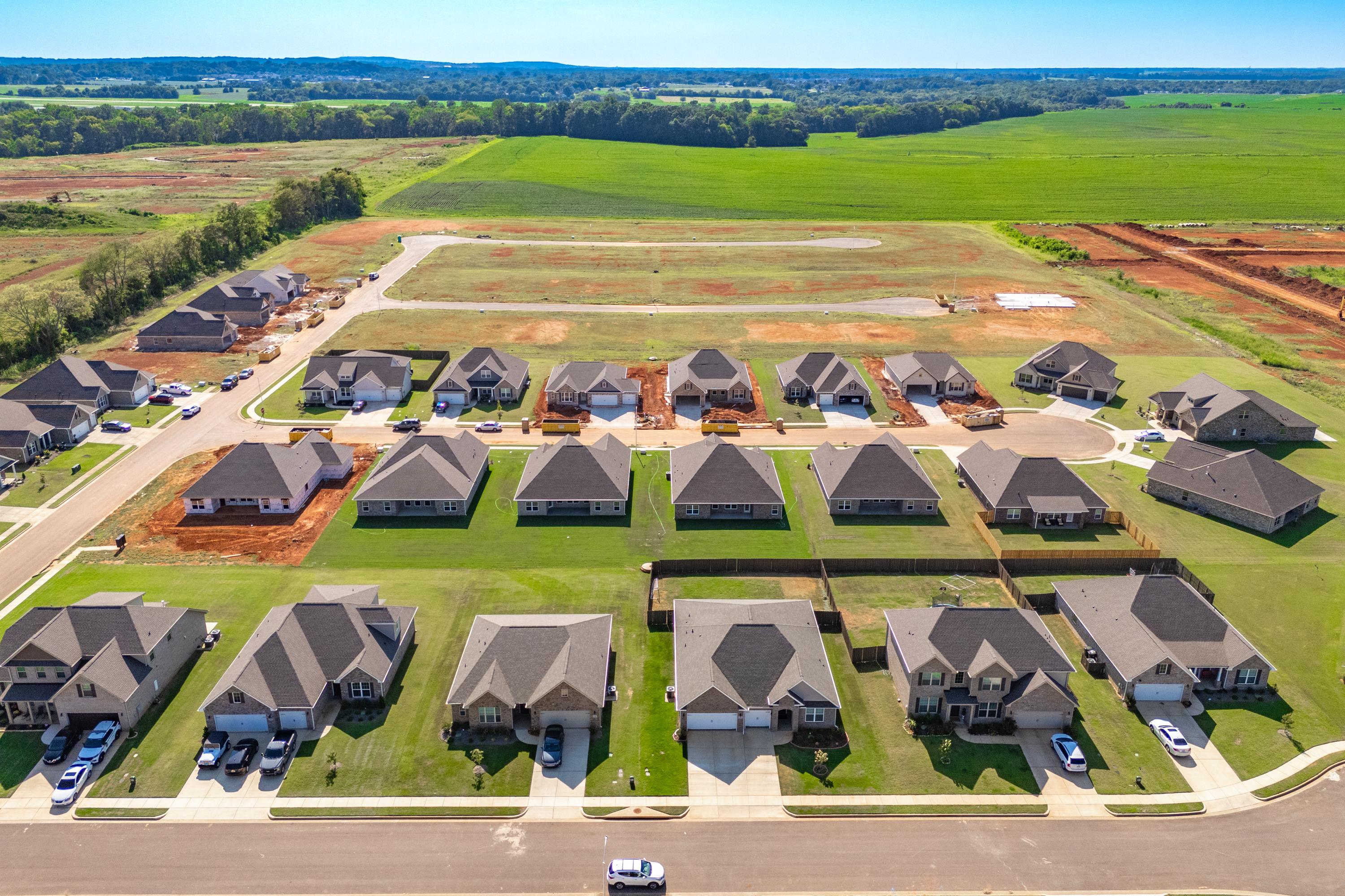 Aerial view of Pikes Ridge neighborhood in Meridianville Alabama featuring new single-family homes with garages amid green lawns and fields