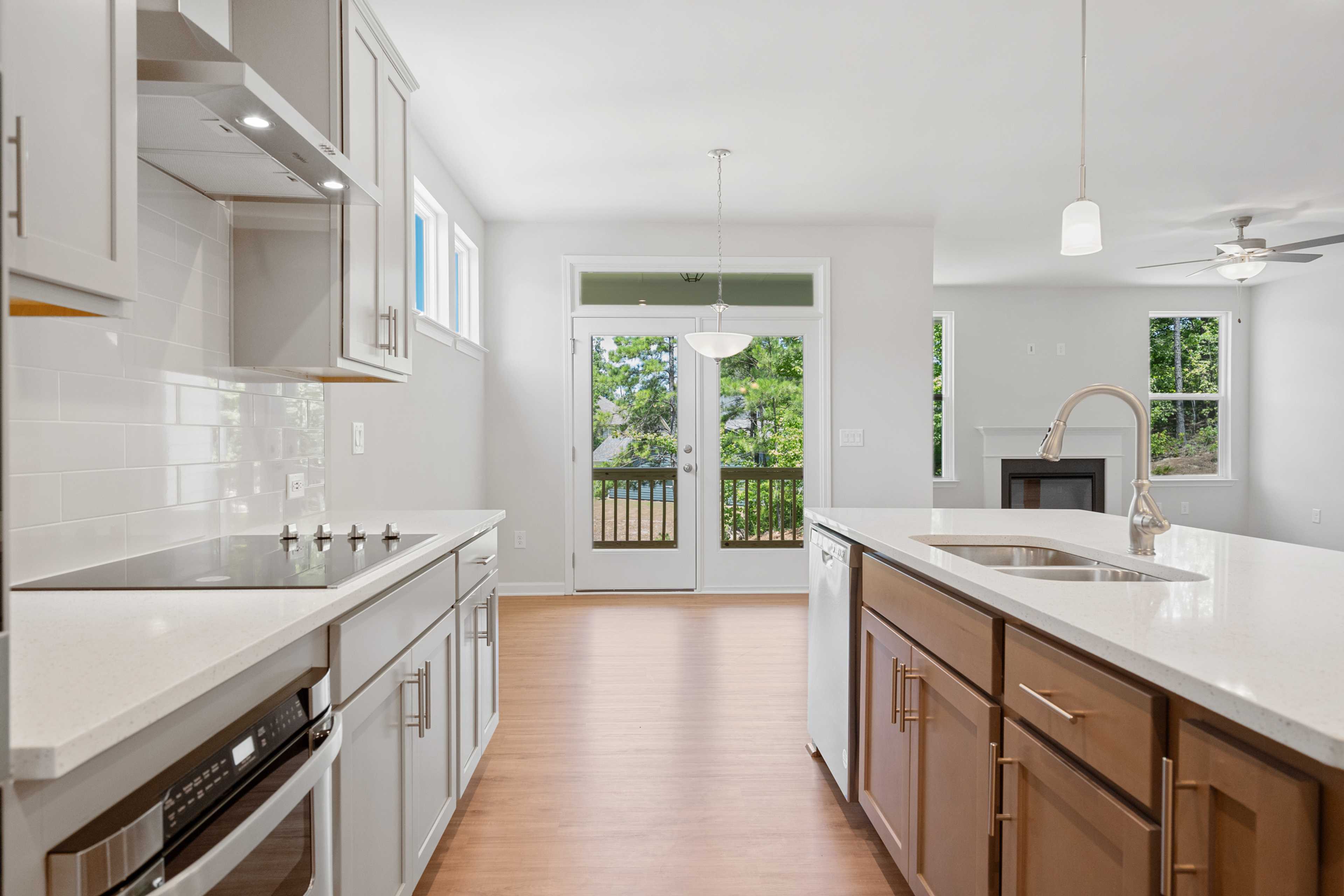 Modern open-concept kitchen at Mountainbrook in Cartersville GA with white shaker cabinets, quartz island, subway tile backsplash, hardwood floors, and French doors to deck