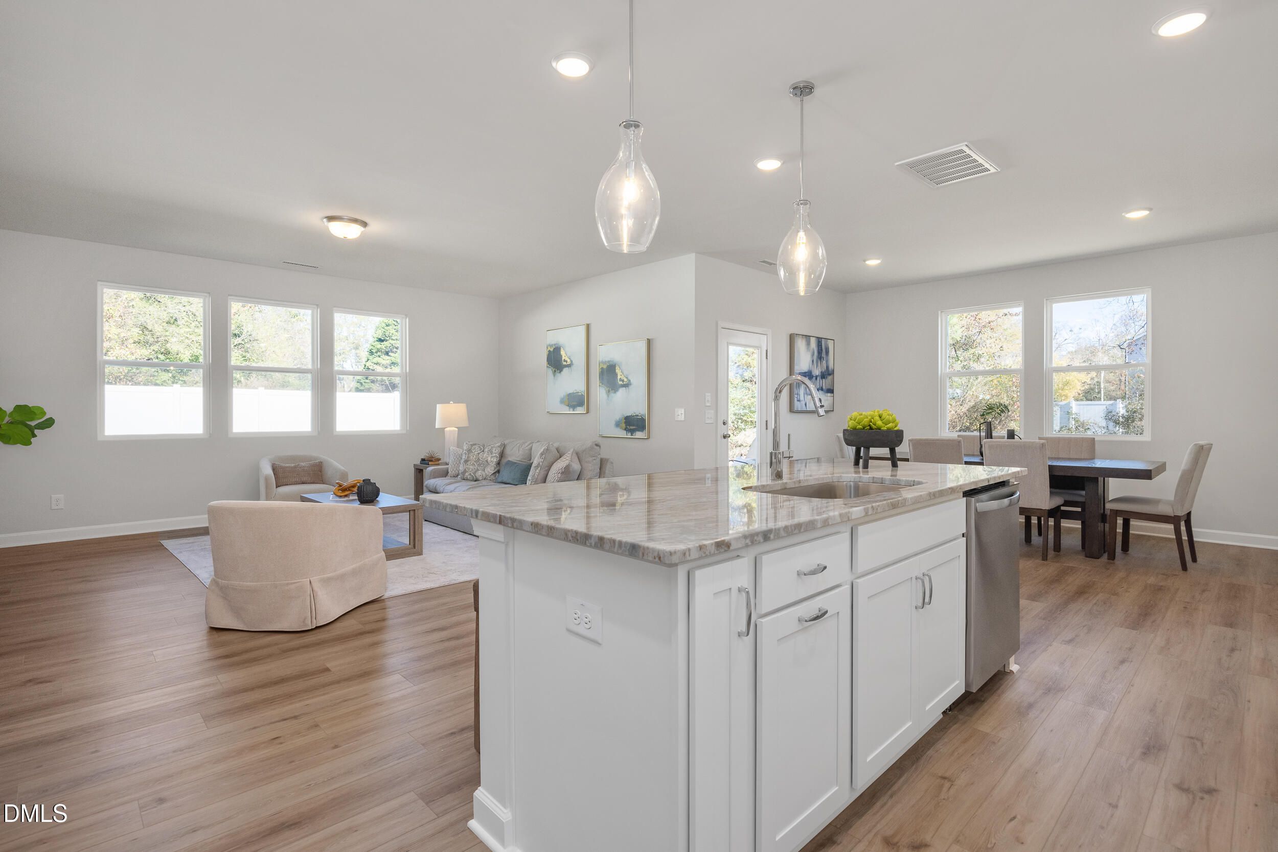 Open-concept kitchen with white cabinets, granite island, and stainless sink adjoining living and dining areas in The Preston C, Lillington, NC