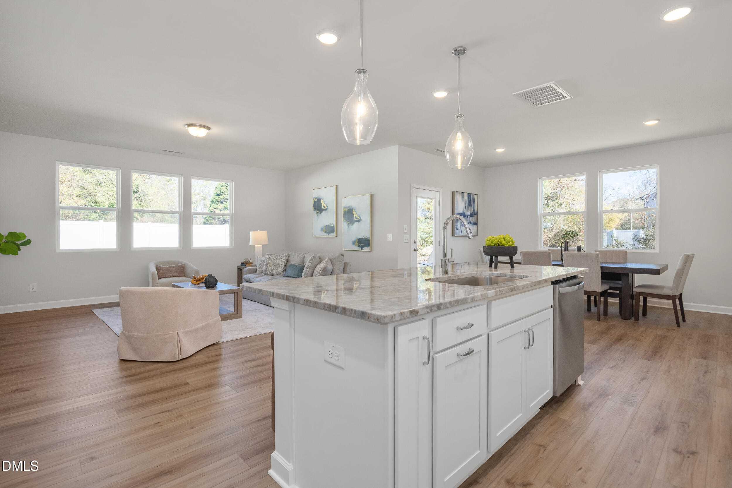Open-concept kitchen with white cabinets, granite island, and stainless sink adjoining living and dining areas in The Preston C, Lillington, NC