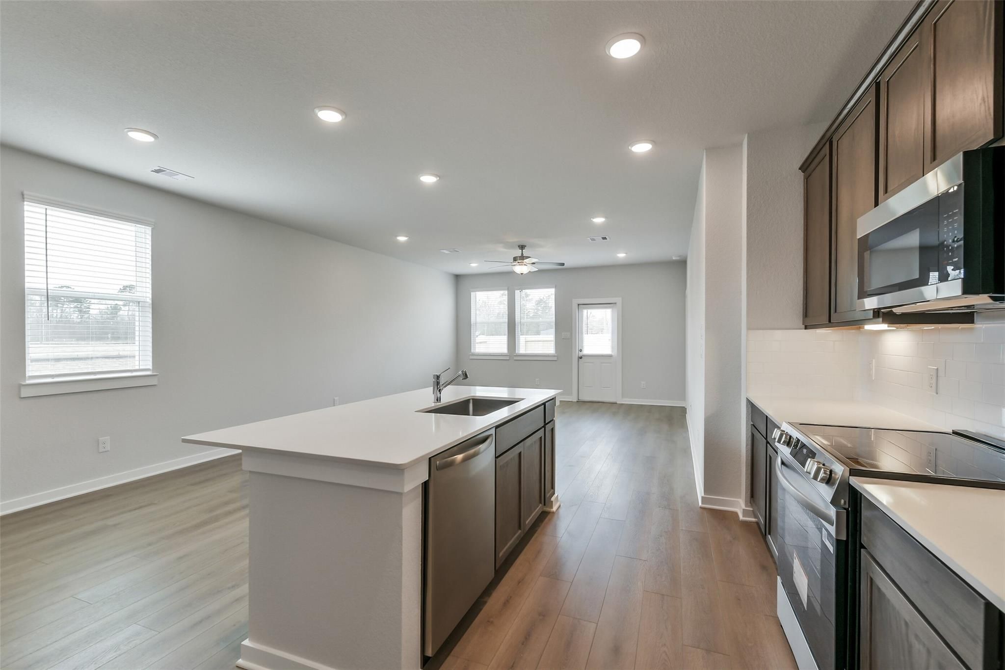 Modern open-concept kitchen featuring white quartz island, stainless steel appliances, and hardwood floors in Davidson Homes The Brazos E, Cleveland Texas