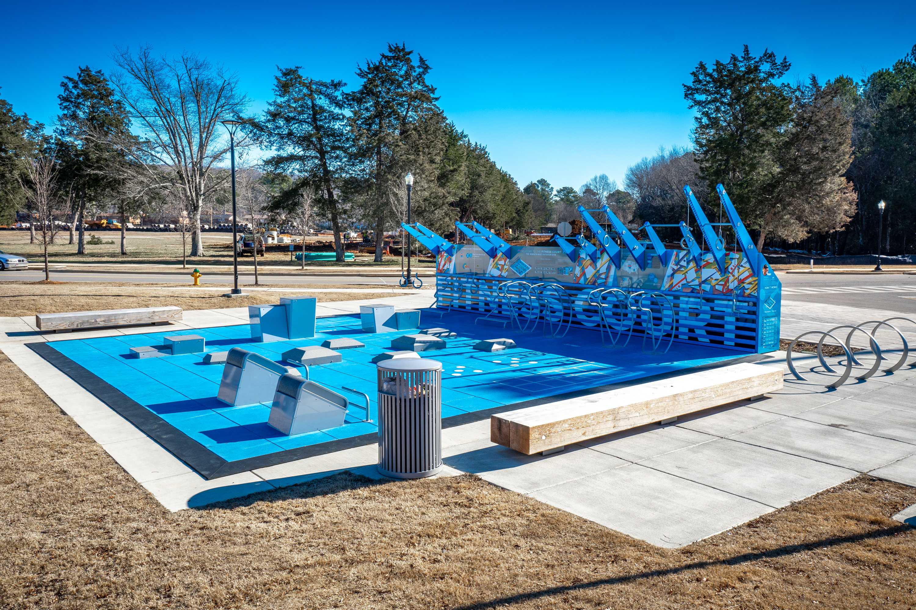 Vibrant blue splash pad at Jaguar Hills in Huntsville Alabama with geometric water structures benches and surrounding trees