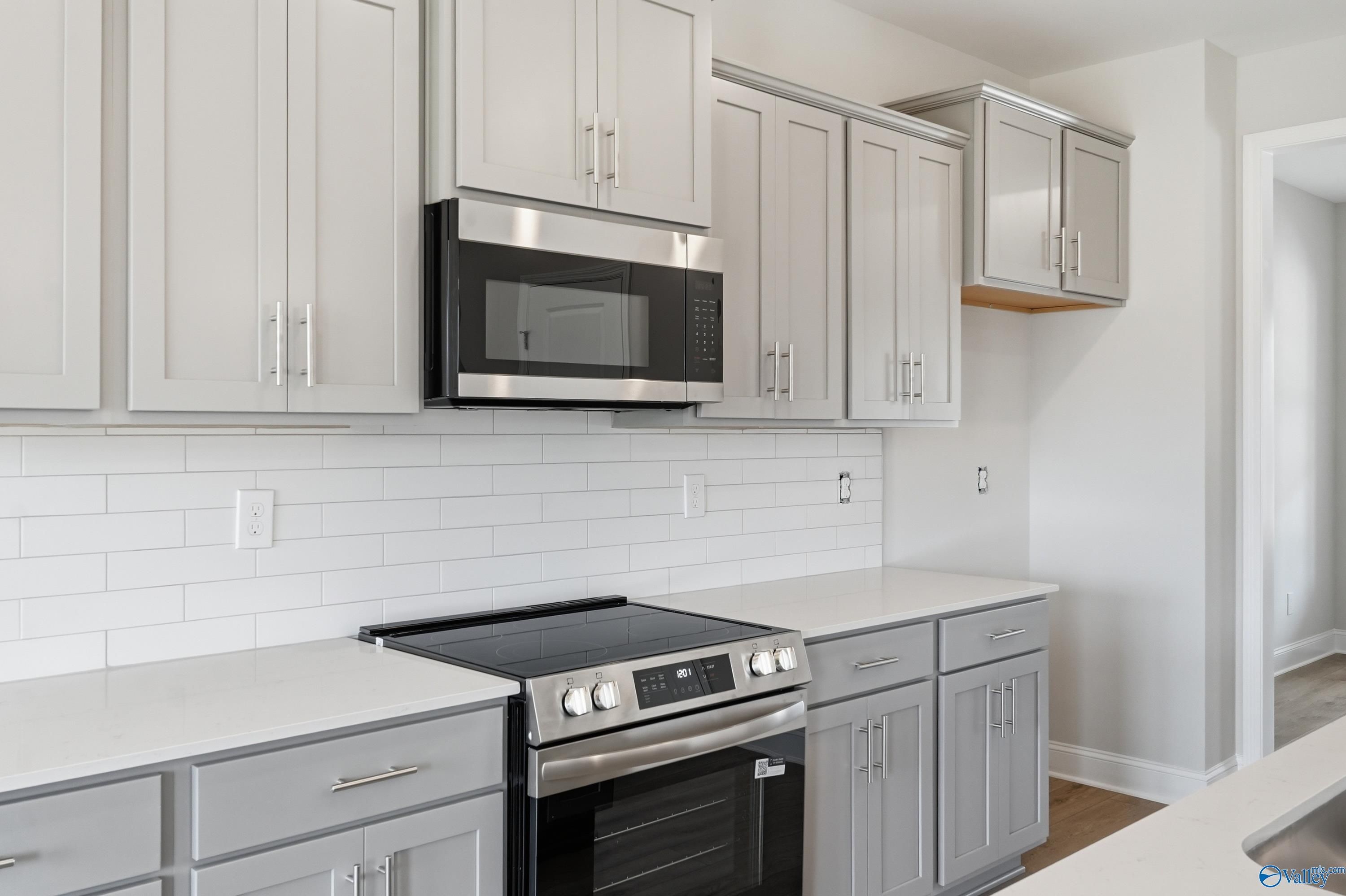 Modern white shaker kitchen cabinets, stainless steel microwave and cooktop, subway tile backsplash in Davidson Homes Shelby B, New Market AL