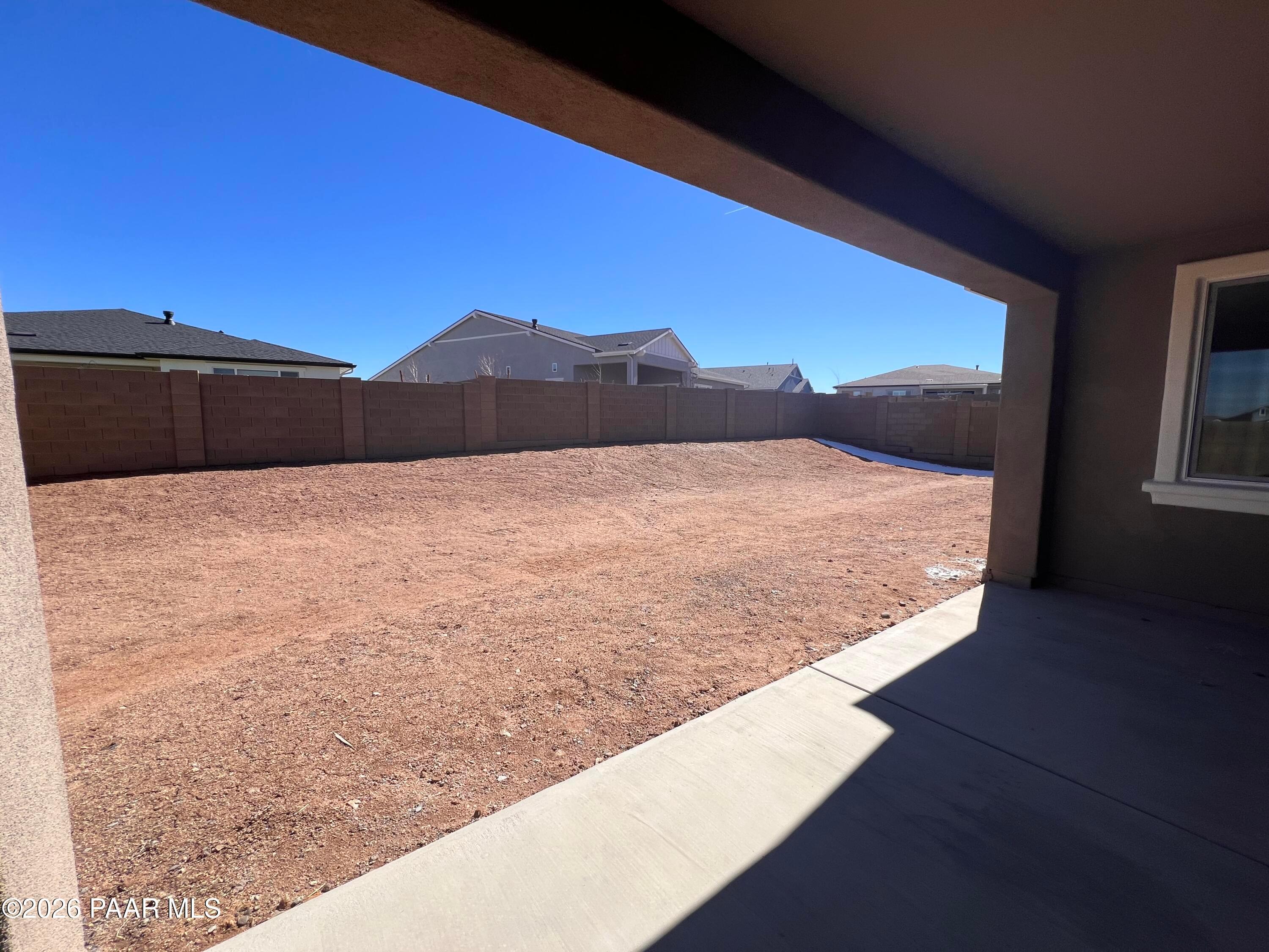 Expansive dirt backyard with tan block fence and neighboring homes under blue sky, from covered patio in Davidson Homes The Sunrise II A, Westwood, Prescott, Arizona