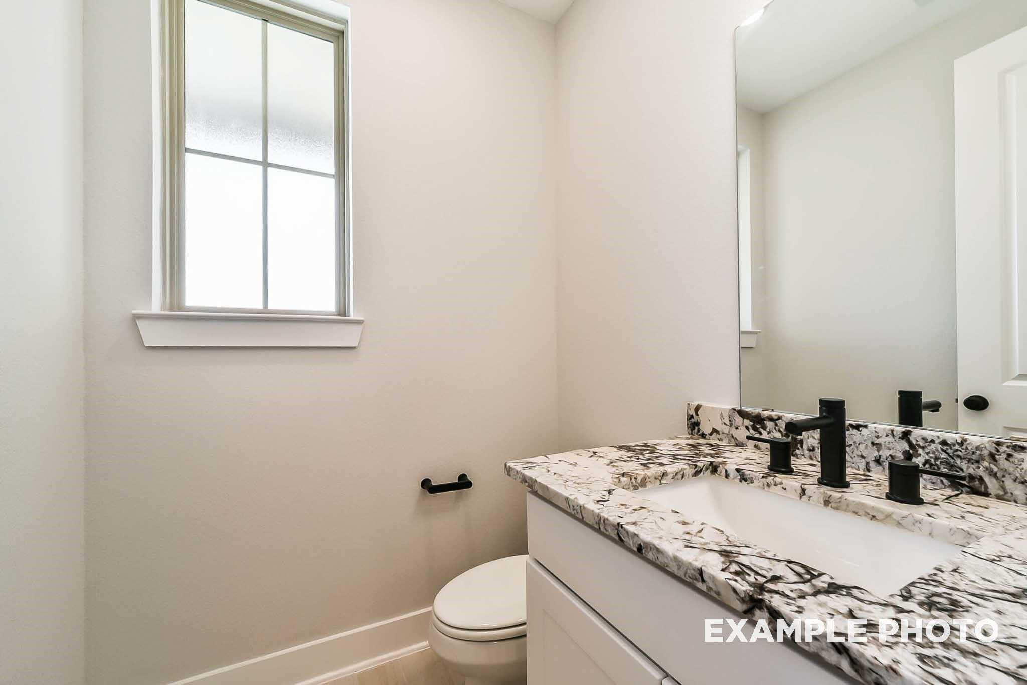 Elegant powder room with marble vanity, black faucet, mirror, and window in Davidson Homes The Philip C, Rosharon, Texas