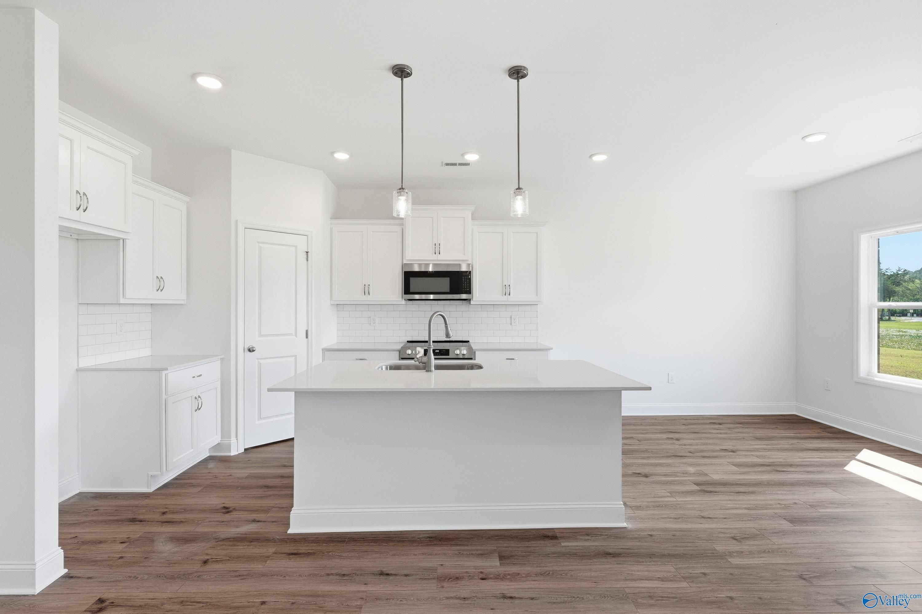 Modern kitchen with white cabinets, center island, and wood flooring in The Asheville floor plan, Jaguar Hills, Huntsville.