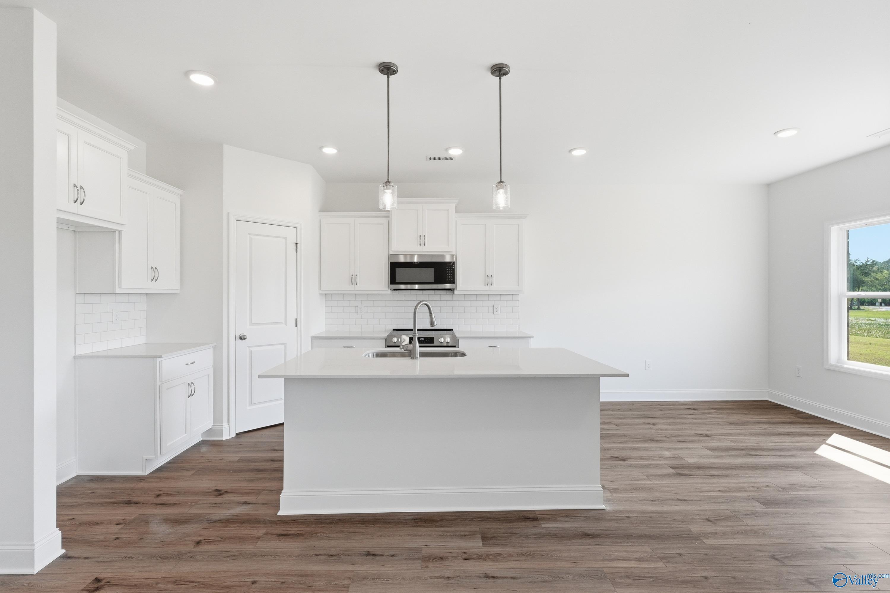 Modern kitchen with white cabinets, center island, and wood flooring in The Asheville floor plan, Jaguar Hills, Huntsville.