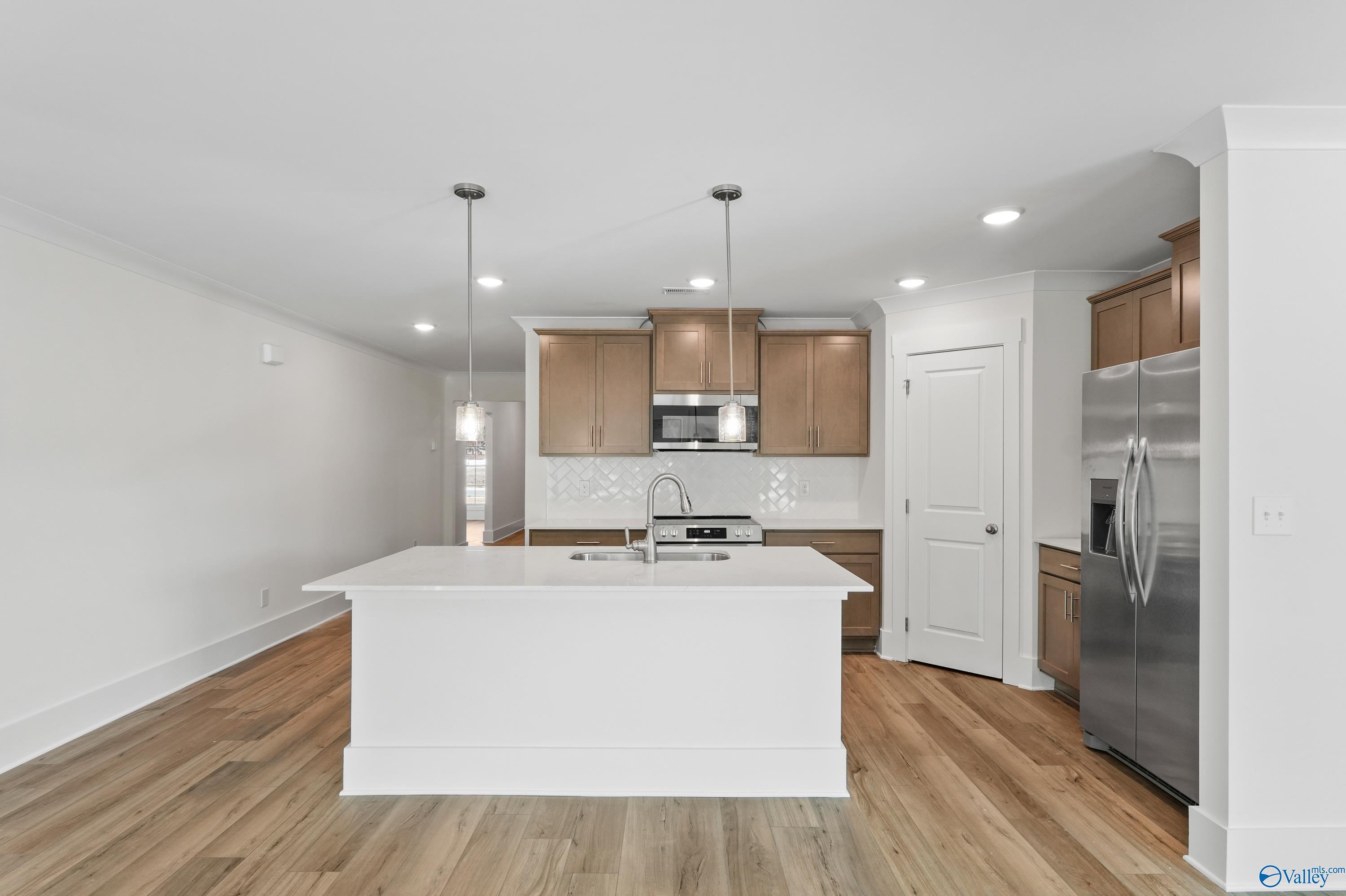 Modern open-concept kitchen with white quartz island, shaker wood cabinets, stainless fridge in Daphne C home, Arab, AL