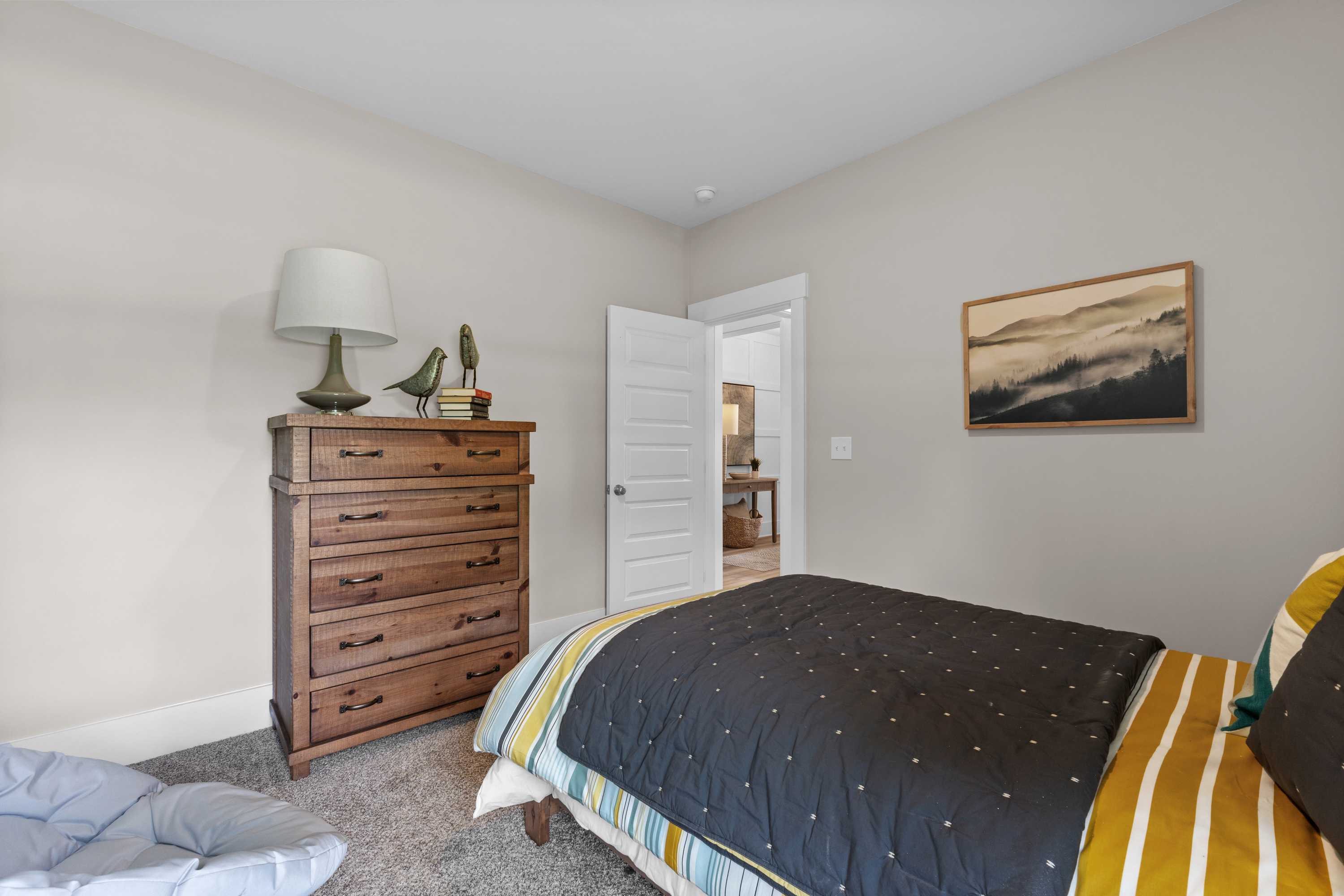 Cozy bedroom at The Highlands in Arab Alabama with wooden dresser lamp bed quilt abstract art and open door