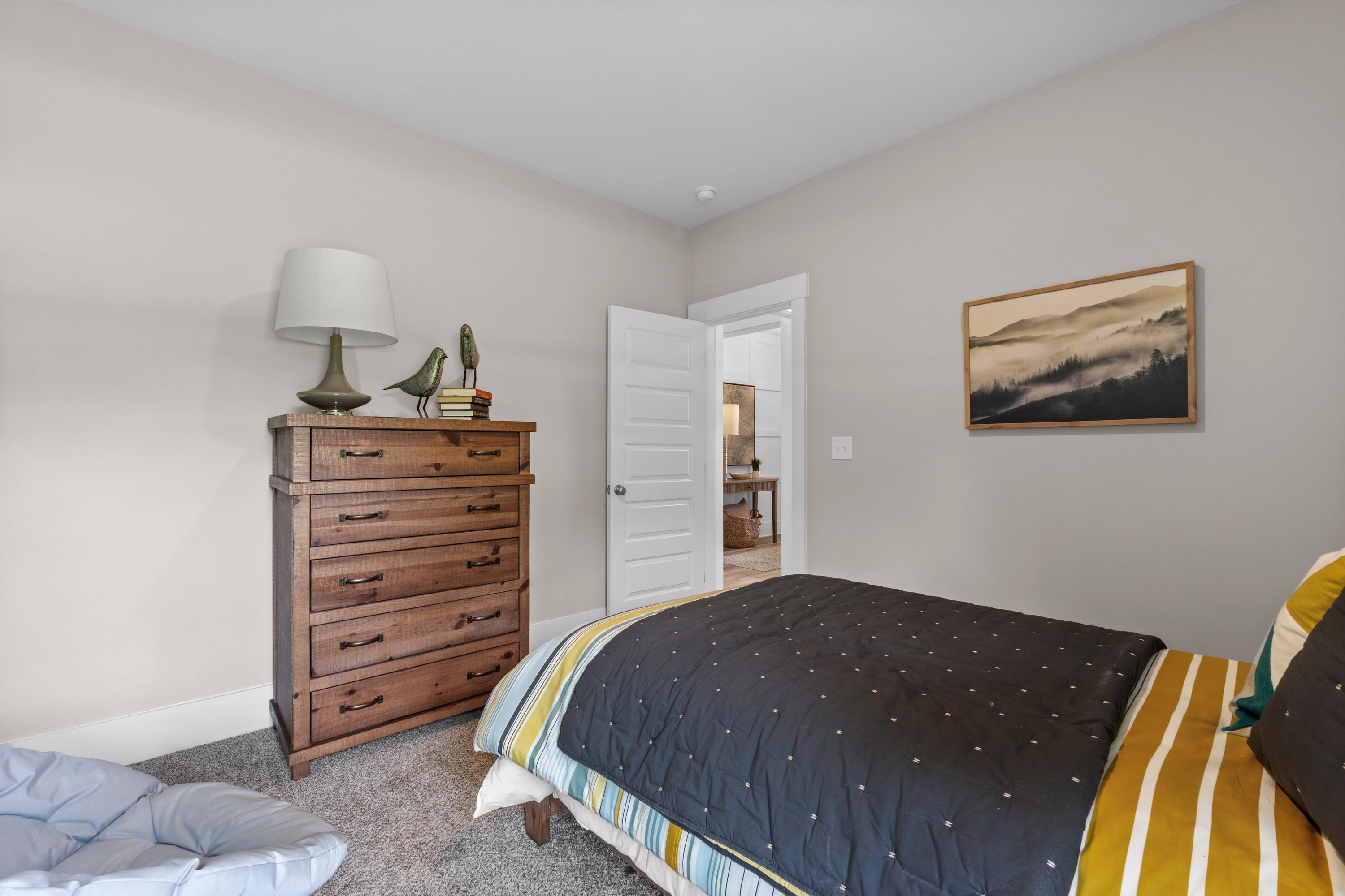 Cozy bedroom at The Highlands in Arab Alabama with wooden dresser lamp bed quilt abstract art and open door