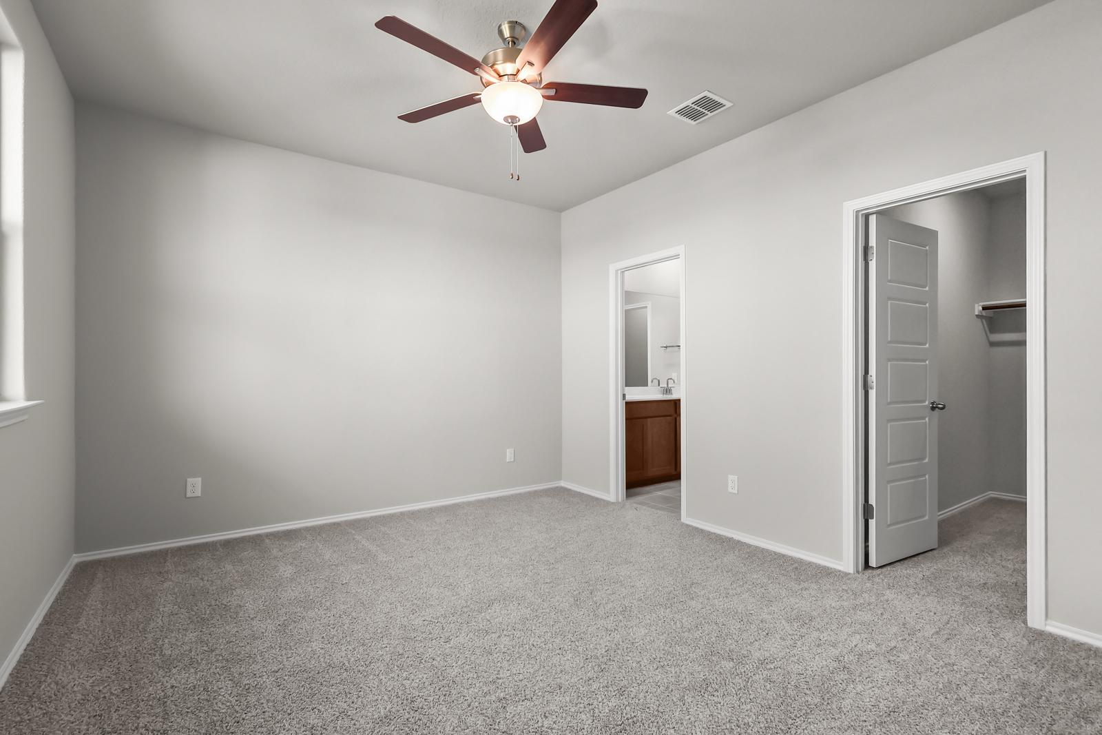 Spacious master bedroom in The Arroyo A featuring neutral carpet, ceiling fan, ensuite bathroom, and walk-in closet.