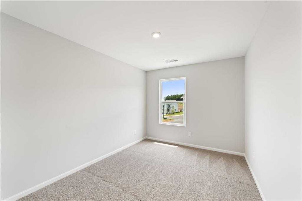 Bright secondary bedroom with gray walls, neutral carpet, and window overlooking trees in Davidson Homes The Monroe A, Emerson, Georgia