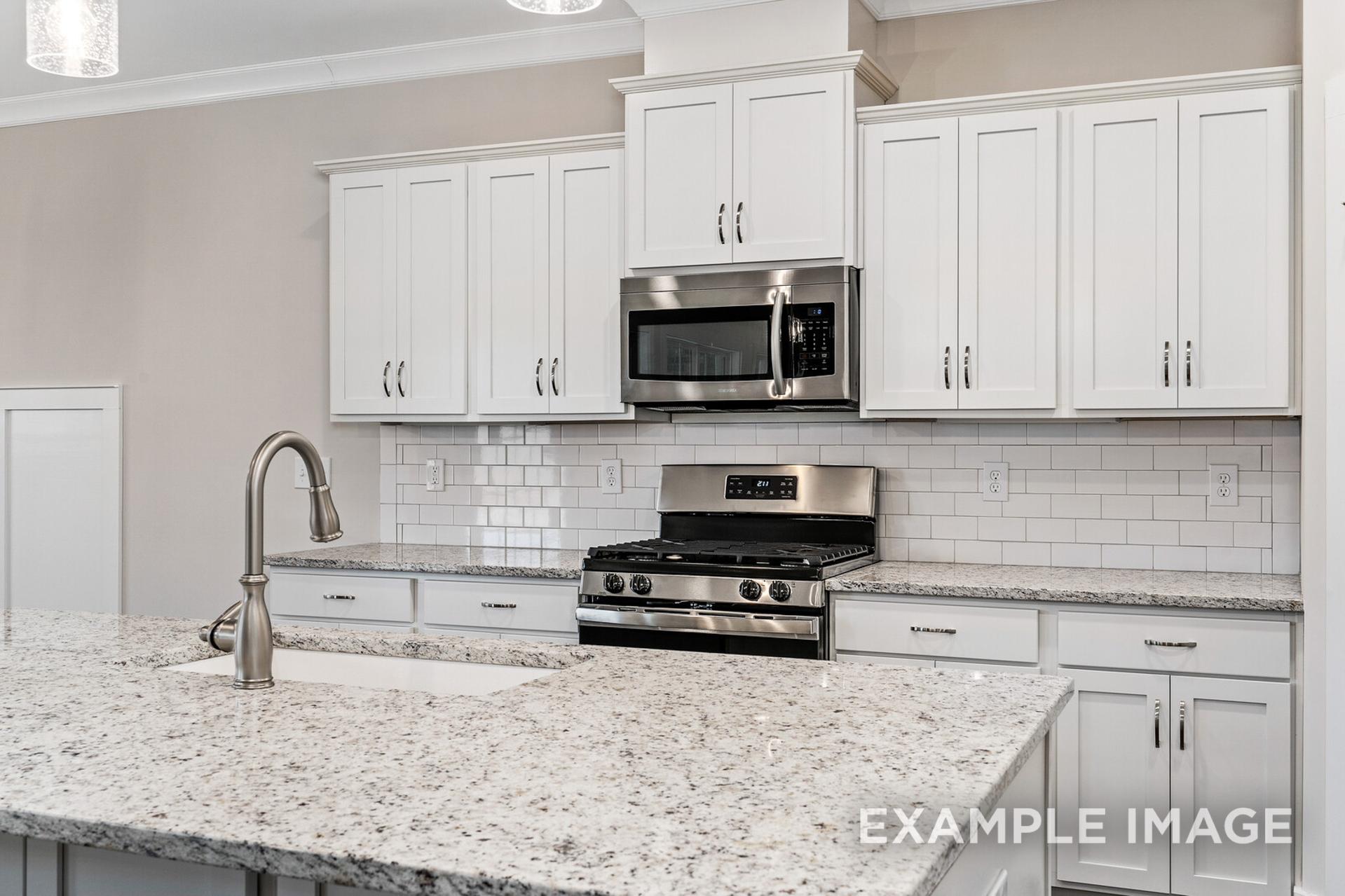 Modern kitchen in The Rockford home with white shaker cabinets, stainless steel appliances, subway tile backsplash, and granite island