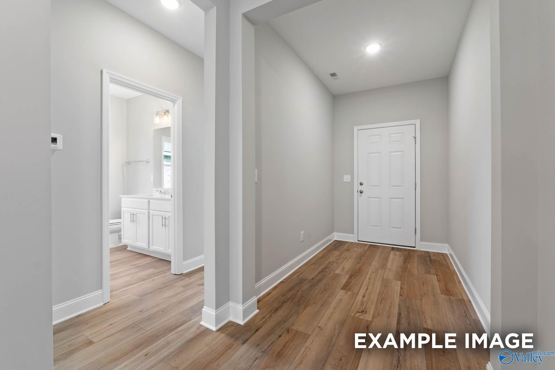 Bright hallway with hardwood floors, white walls, and guest bathroom featuring white vanity in Davidson Homes The Everett B, Hazel Green, Alabama