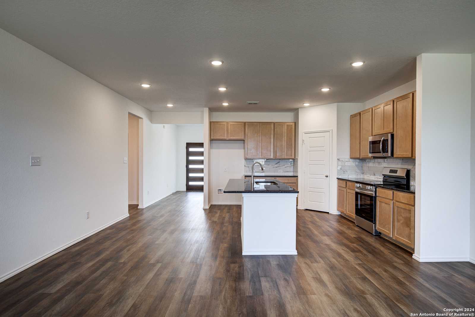 Modern open-concept kitchen with oak cabinets, granite island sink, stainless appliances and hardwood floors in The Douglas D, Seguin, TX