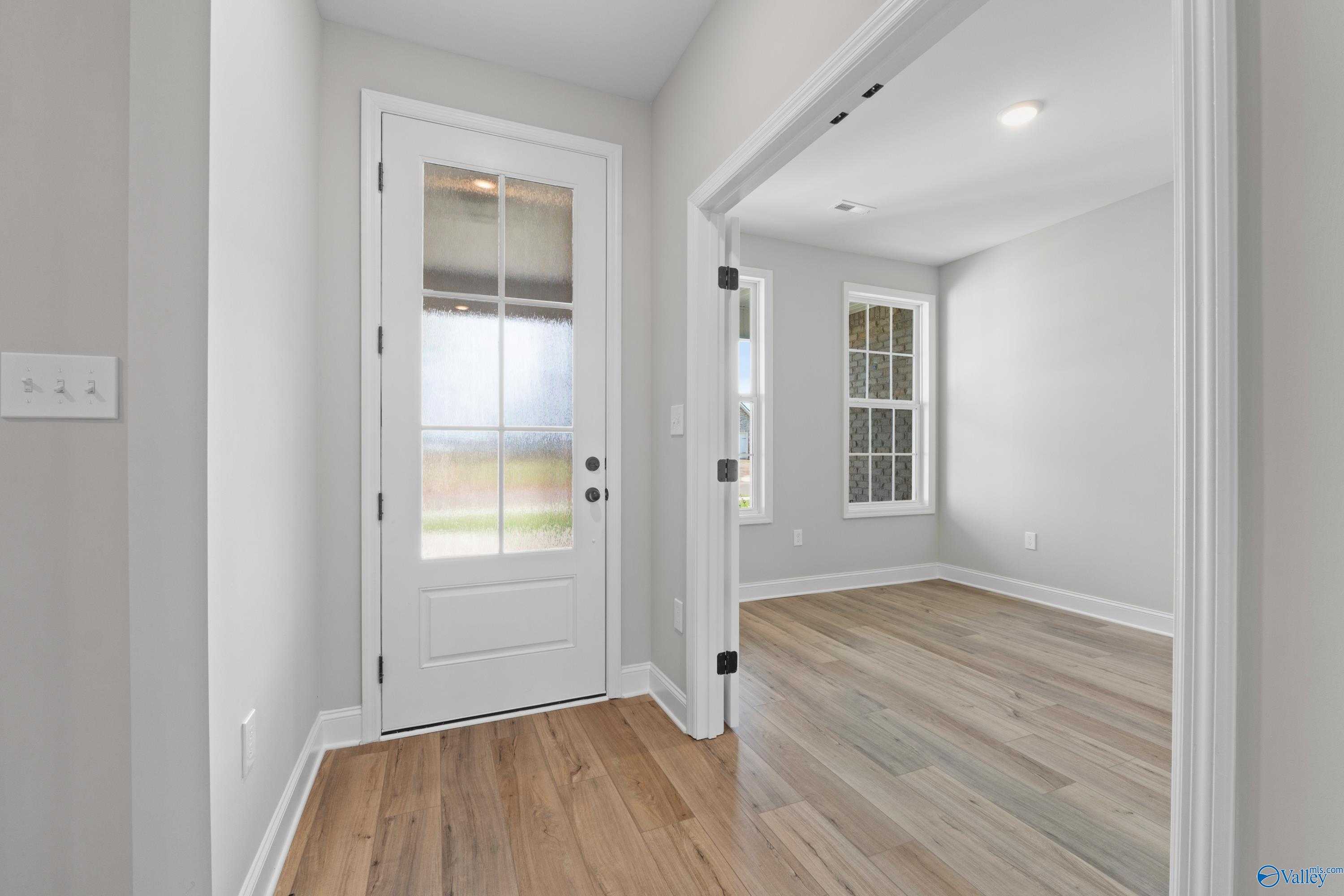 Bright entry foyer with white glass-pane door, open archway, hardwood floors, and natural light in Davidson Homes The Rockford, Toney, AL