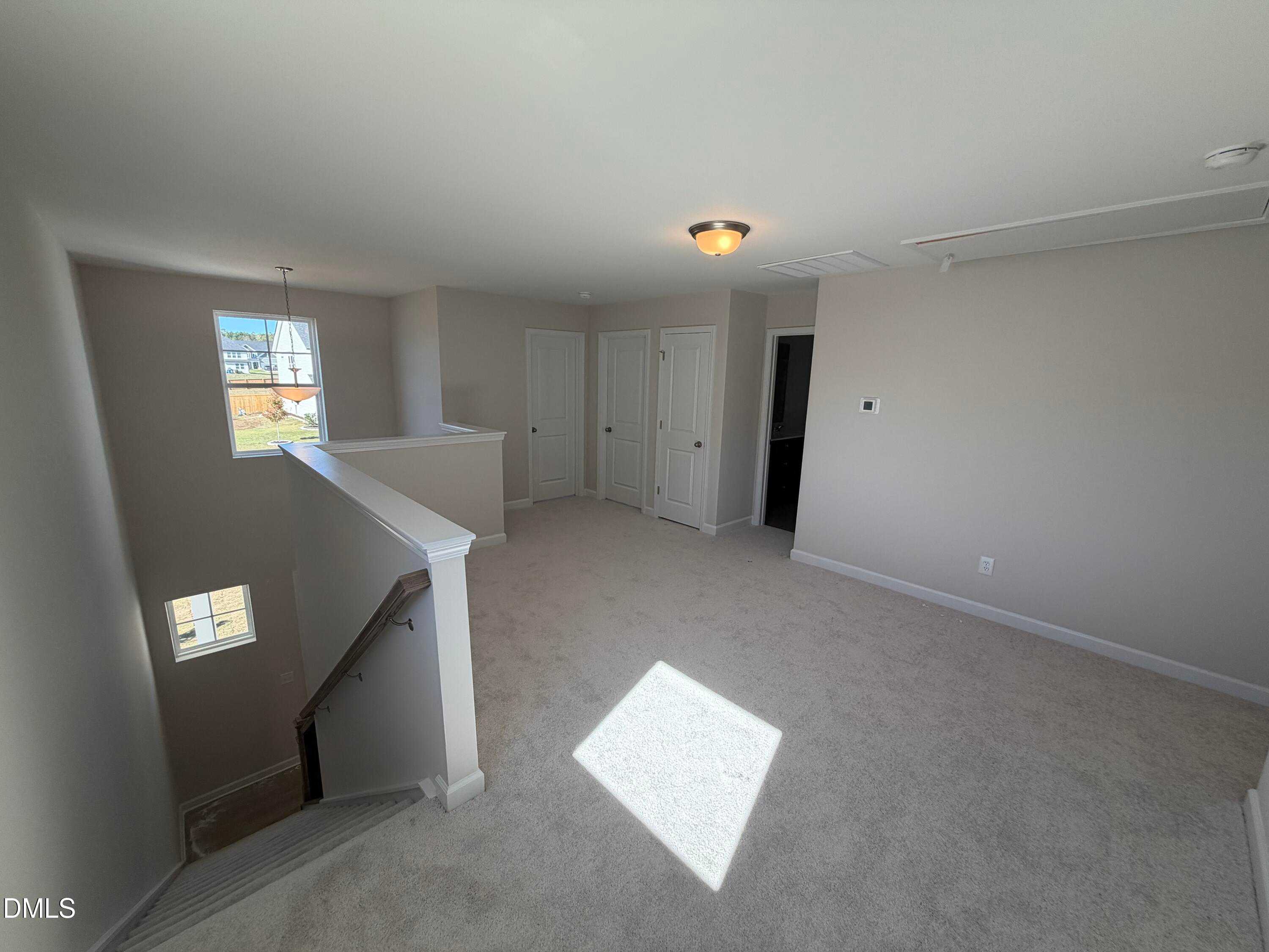 Bright upstairs hallway with beige carpet, wooden railing staircase, and bedroom doors in The Gavin C floor plan, Lillington, NC