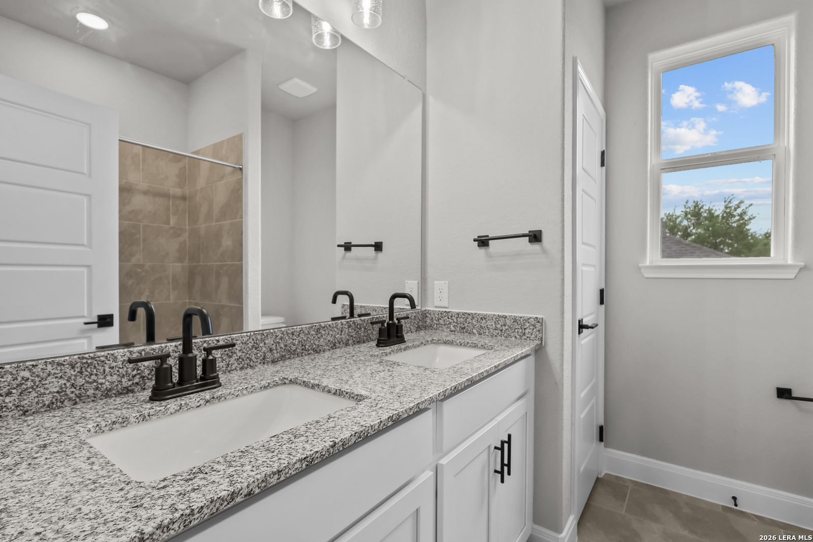 Elegant master bathroom featuring double granite vanity, black faucets, walk-in shower in Davidson Homes The Belmont H, Castroville, Texas