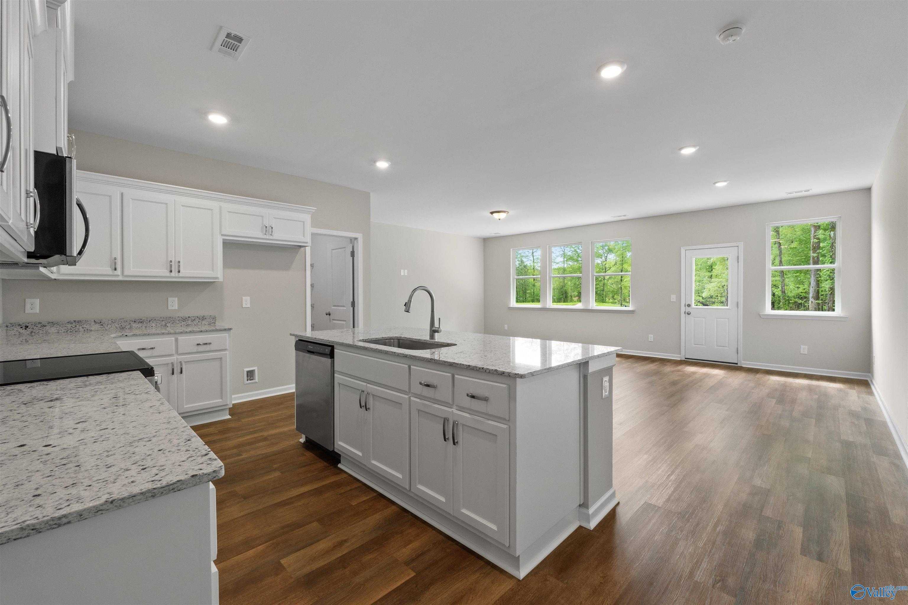 Modern open-concept kitchen featuring white cabinets, granite countertops, center island sink, and stainless dishwasher in The Luna by Davidson Homes, Hazel Green, AL