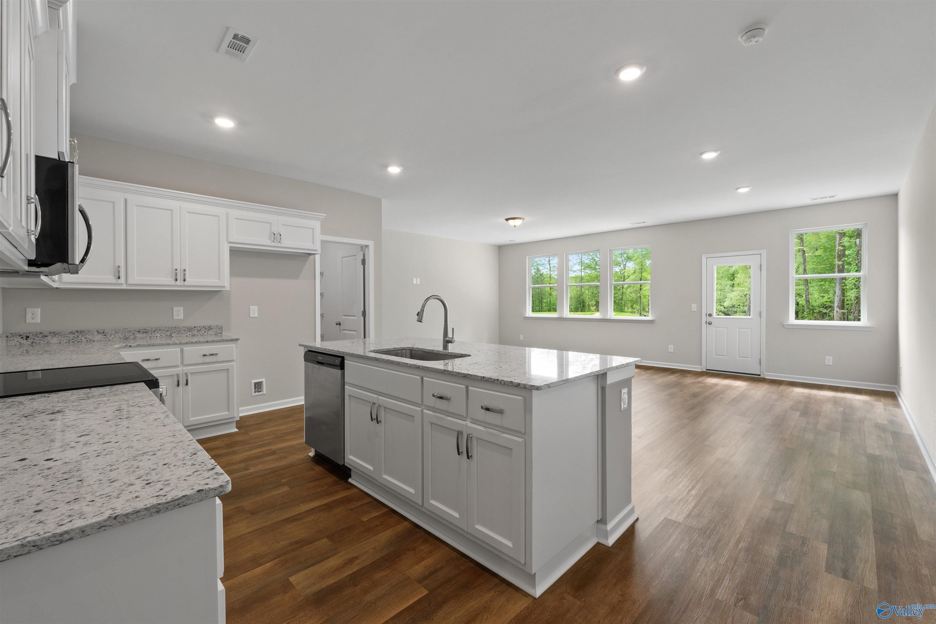Modern open-concept kitchen featuring white cabinets, granite countertops, center island sink, and stainless dishwasher in The Luna by Davidson Homes, Hazel Green, AL
