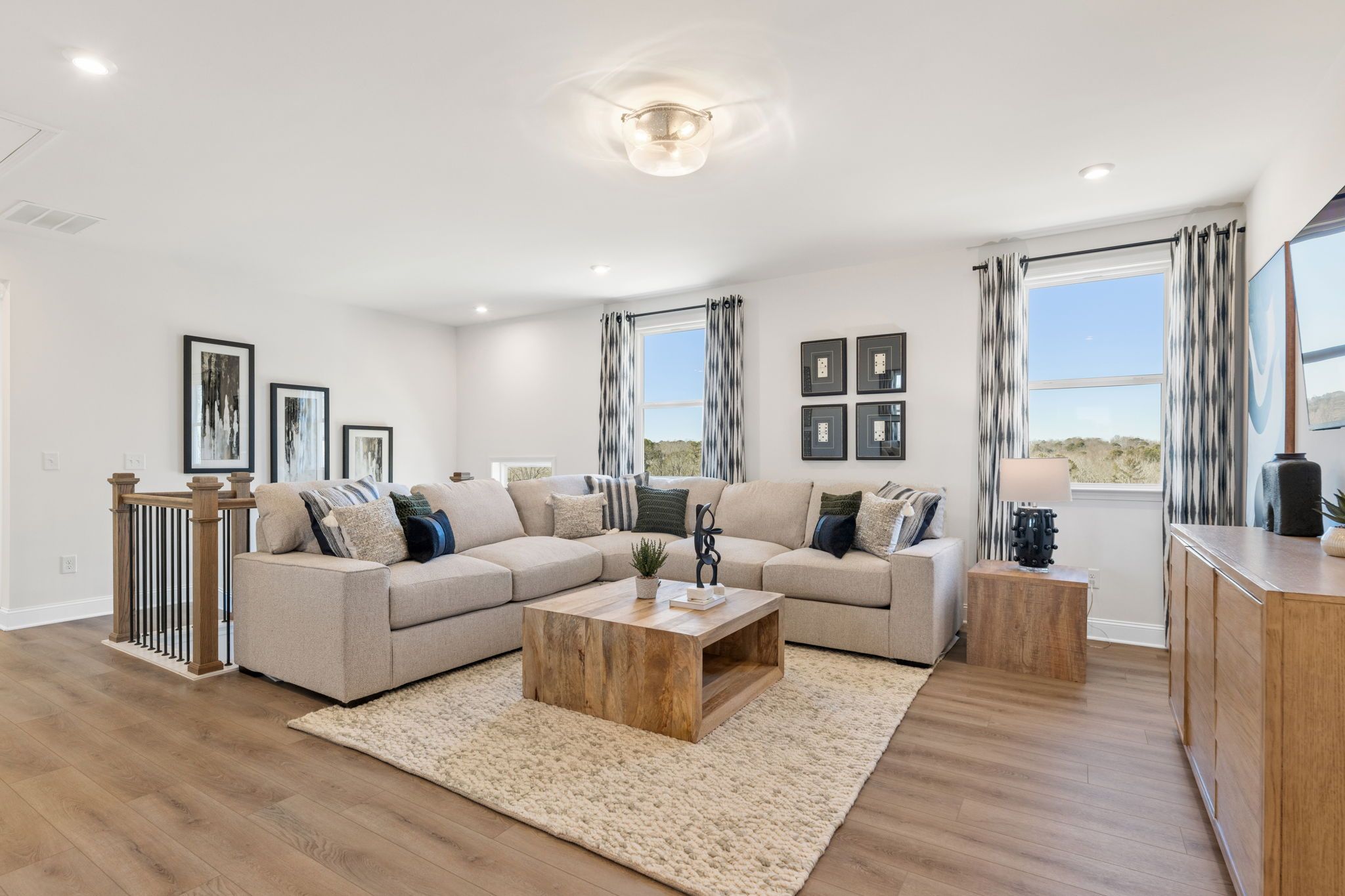 Open-concept living room at Fern Hollow in Buford GA with beige L-shaped sofa, hardwood floors, and large windows