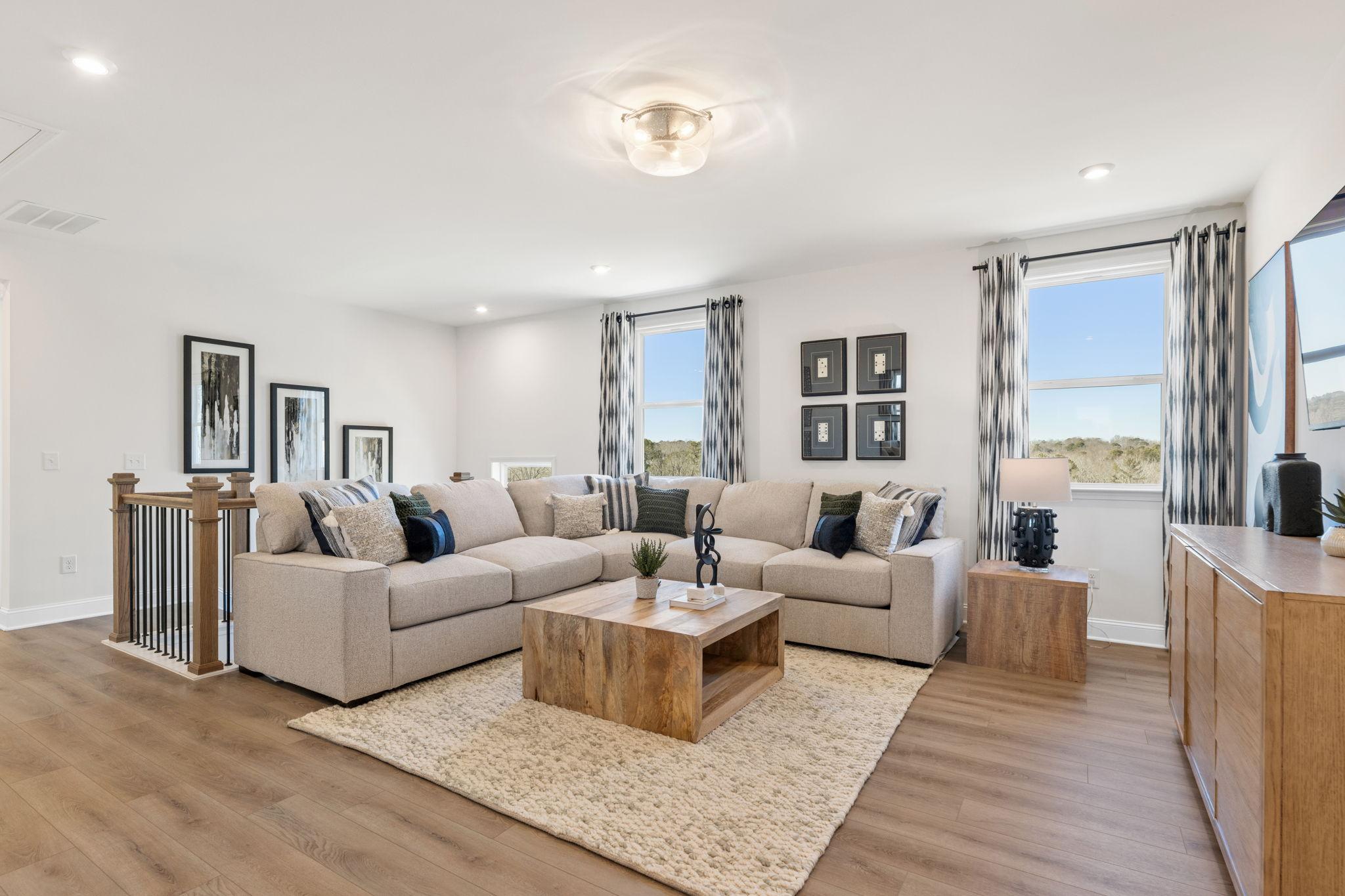 Open-concept living room at Fern Hollow in Buford GA with beige L-shaped sofa, hardwood floors, and large windows