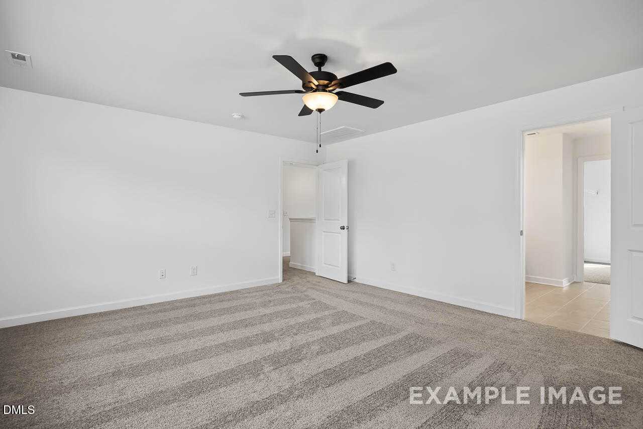 Spacious empty bedroom with ceiling fan, beige striped carpet, and open doorways in Davidson Homes The Willow D, Zebulon, NC