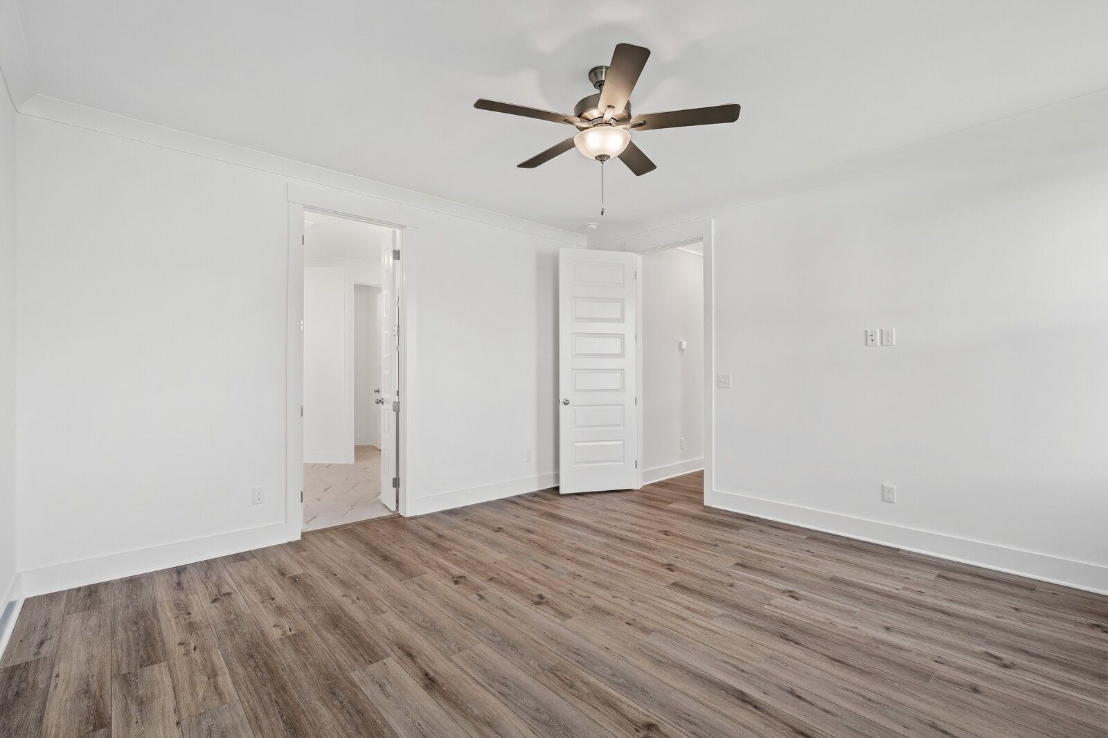 Spacious bedroom with hardwood floors, white walls, ceiling fan, and open doors in Davidson Homes The Hawkins, Murfreesboro TN