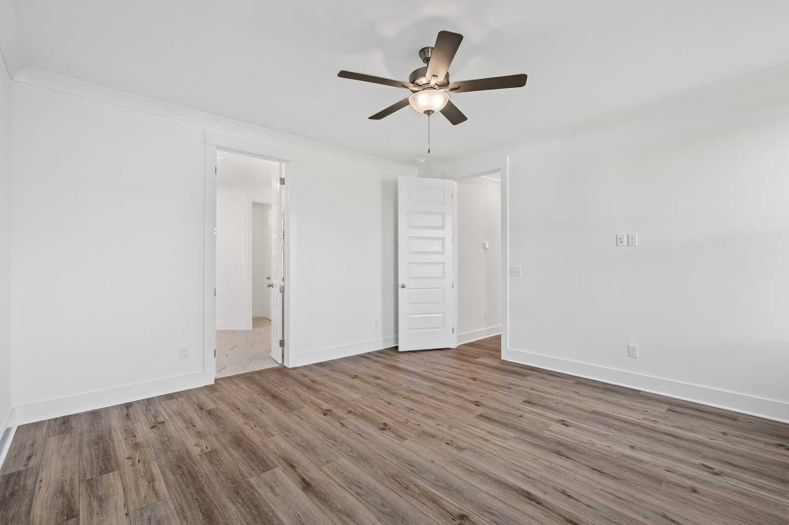 Spacious bedroom with hardwood floors, white walls, ceiling fan, and open doors in Davidson Homes The Hawkins, Murfreesboro TN