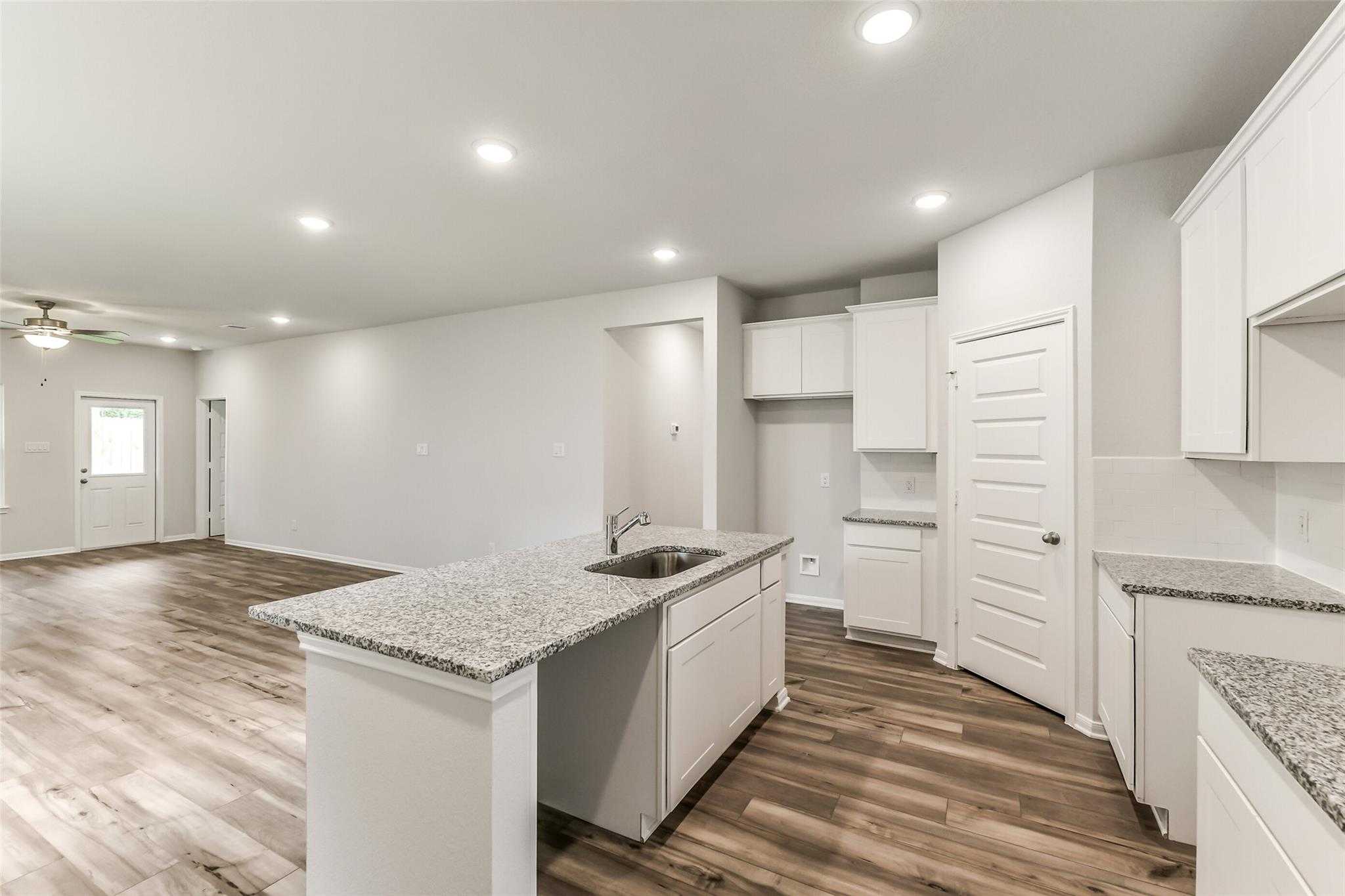 Open-concept kitchen with white cabinets, granite island sink, hardwood floors, and ceiling fan in Sabine F home, Conroe, Texas