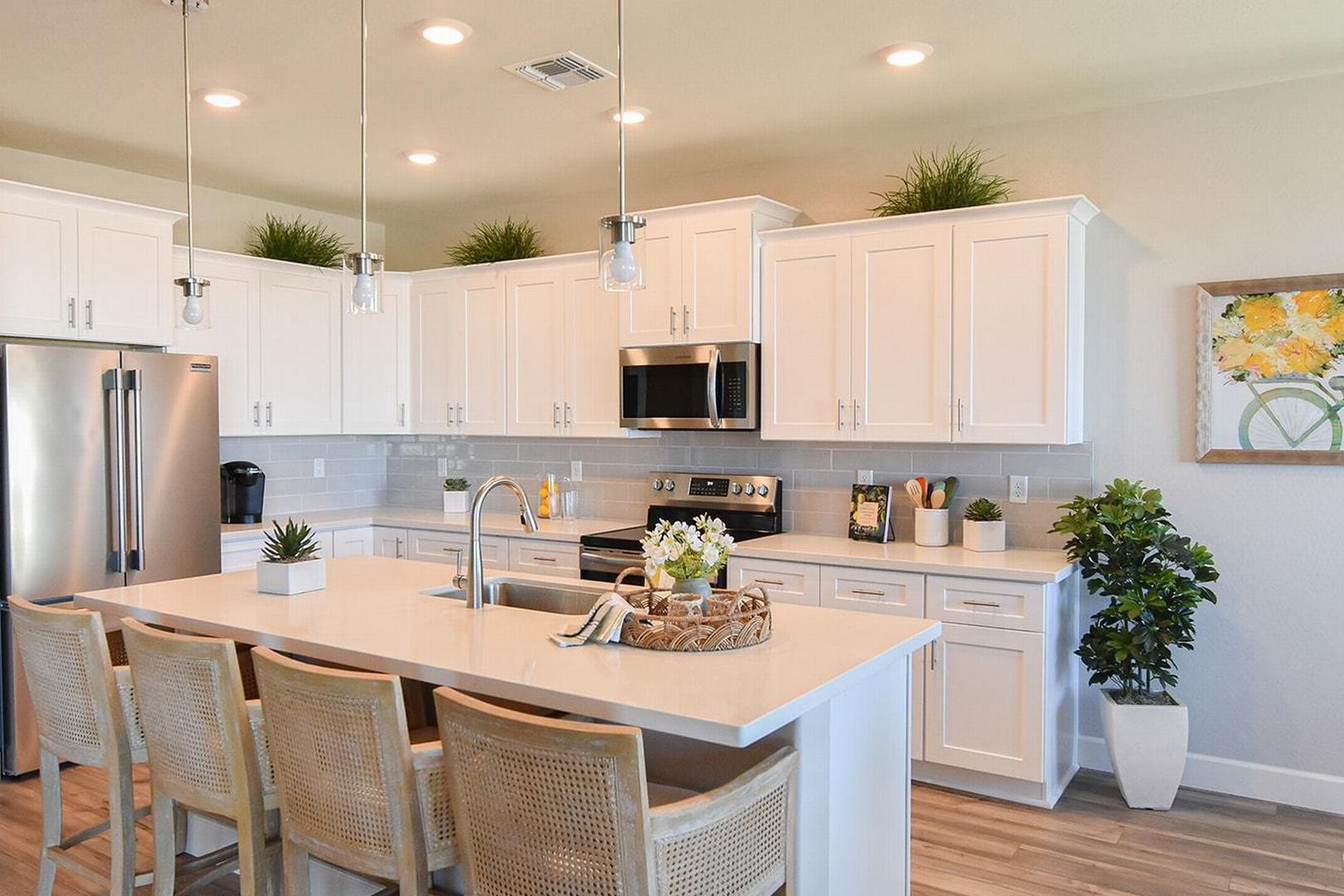 Spacious kitchen in The Summit E with white shaker cabinets, stainless steel appliances, large center island, and potted plants