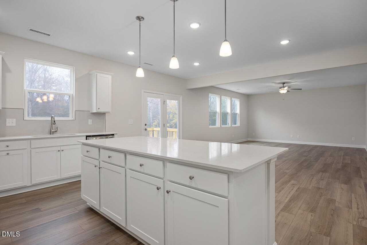 Modern white kitchen with quartz island, pendant lights, and French doors to backyard in The Hickory II A, Lillington, NC