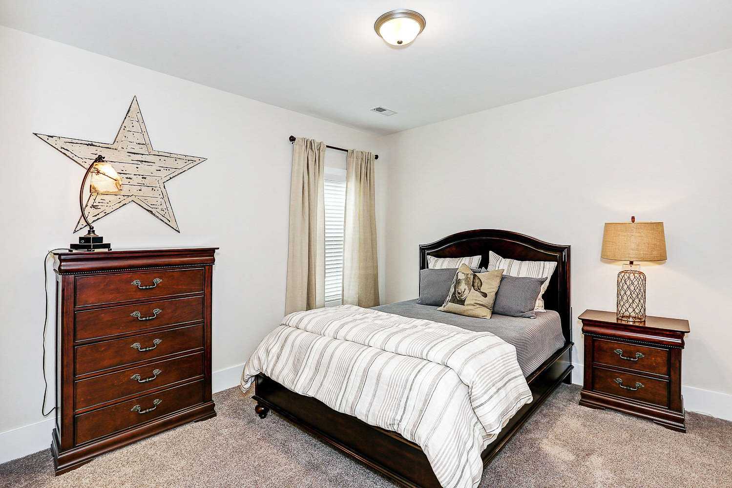Cozy bedroom in The Finleigh featuring wooden dresser, king bed with striped duvet, lamps, and star decor