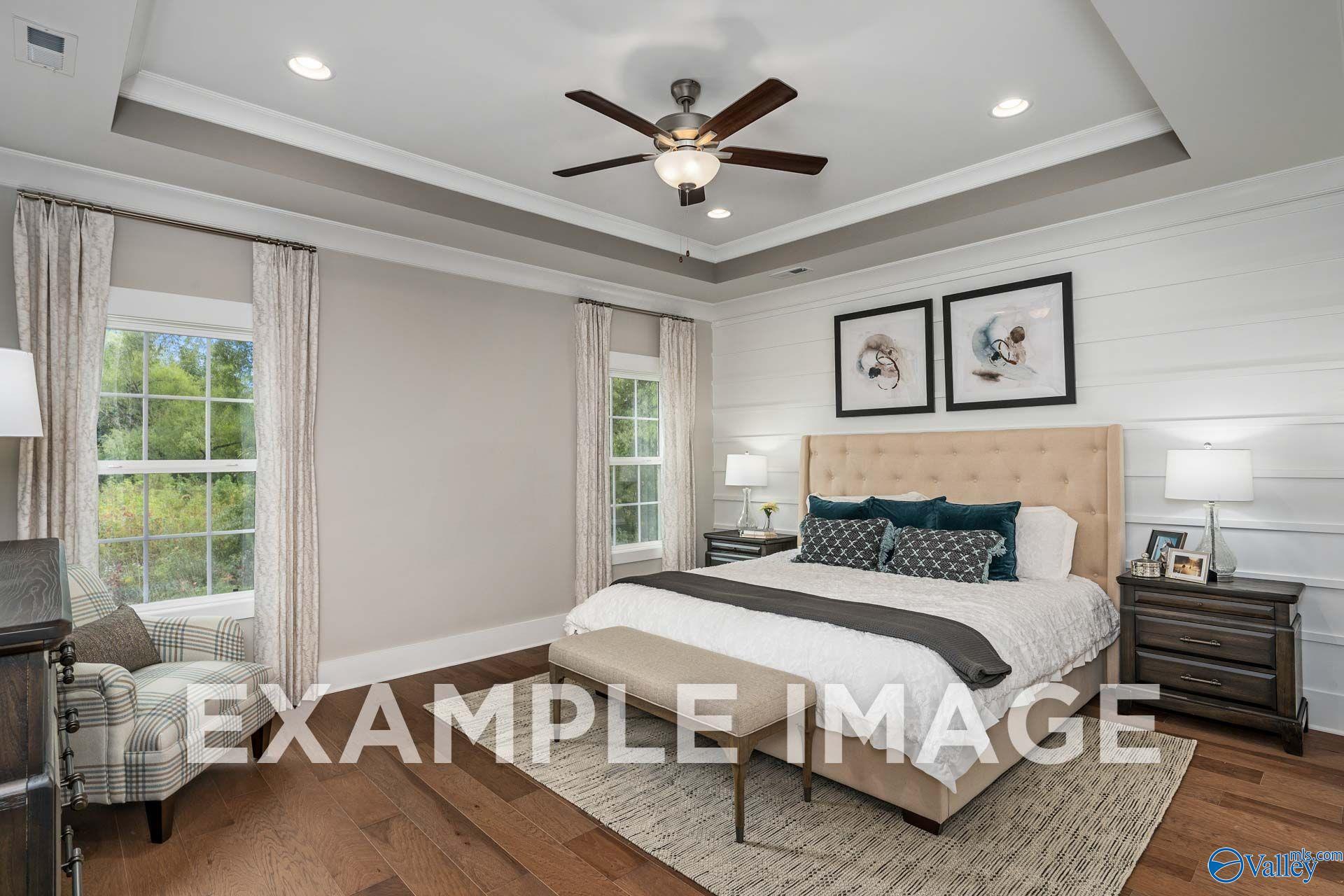 Elegant master bedroom with tray ceiling, shiplap accent wall, and hardwood floors in Davidson Homes The Harrison, Hartselle, Alabama