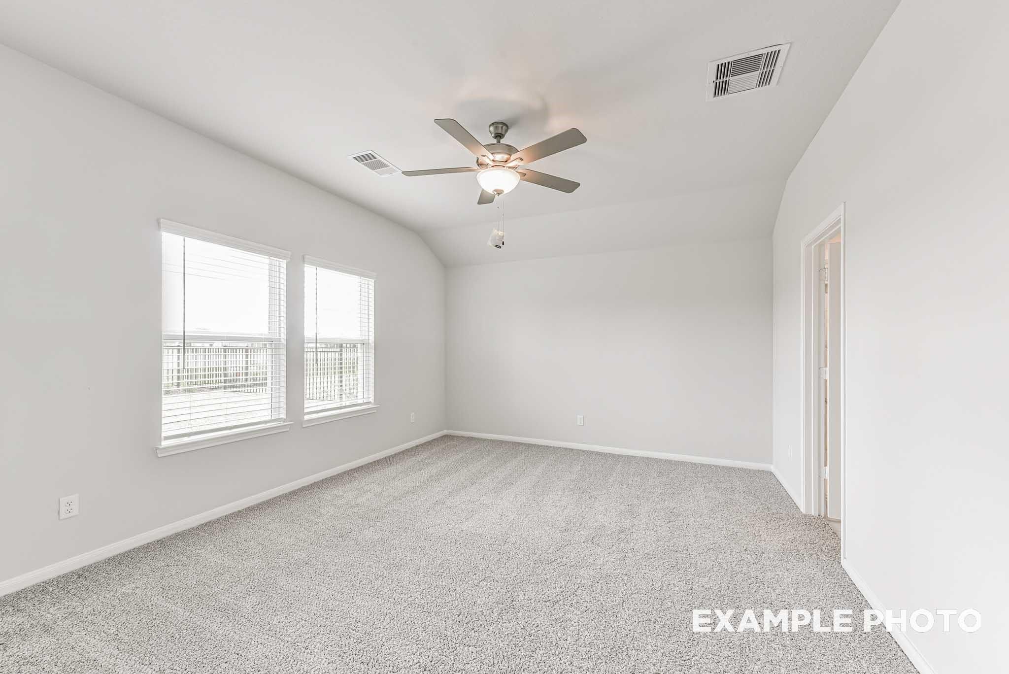 Bright empty bedroom with large windows, ceiling fan, and gray carpet in Davidson Homes Riviera A, Rosharon, Texas
