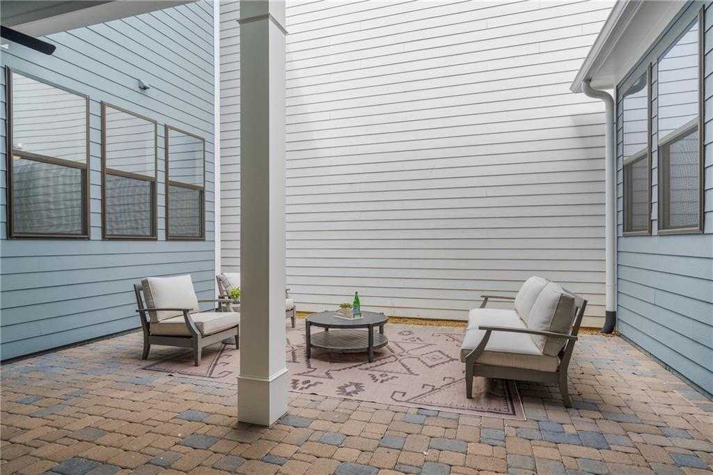 Screened porch with white wicker seating, coffee table, and rug on brick pavers in Davidson Homes Seaside B, Woodstock, Georgia